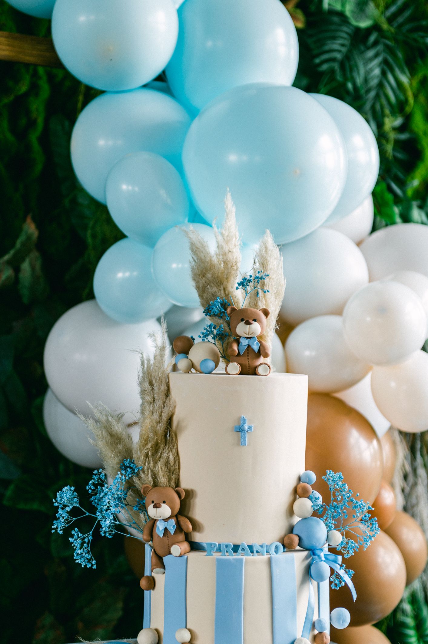 Baby blue and white balloon arch with teddy bear decorated cake for baby shower celebration.