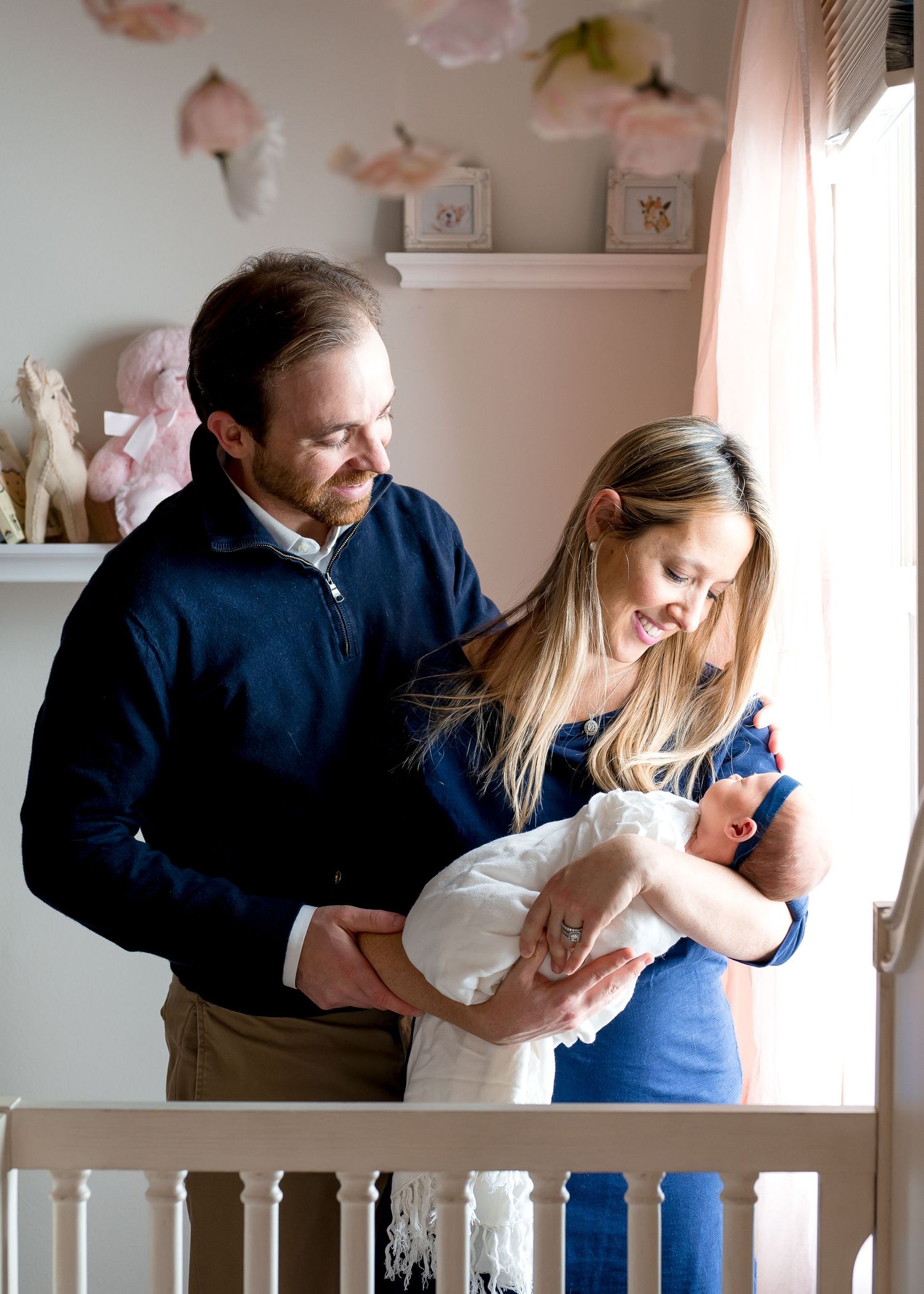 father and mother smiling at their newborn baby girl inside her pink soft nursery in west u in houston