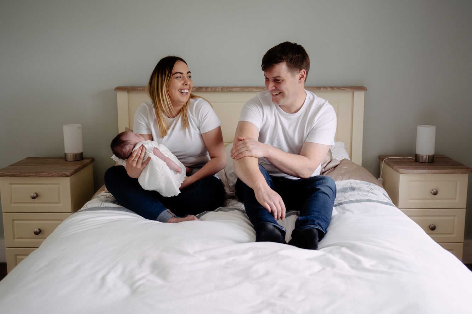 Family sitting together on white bed with matching outfits.