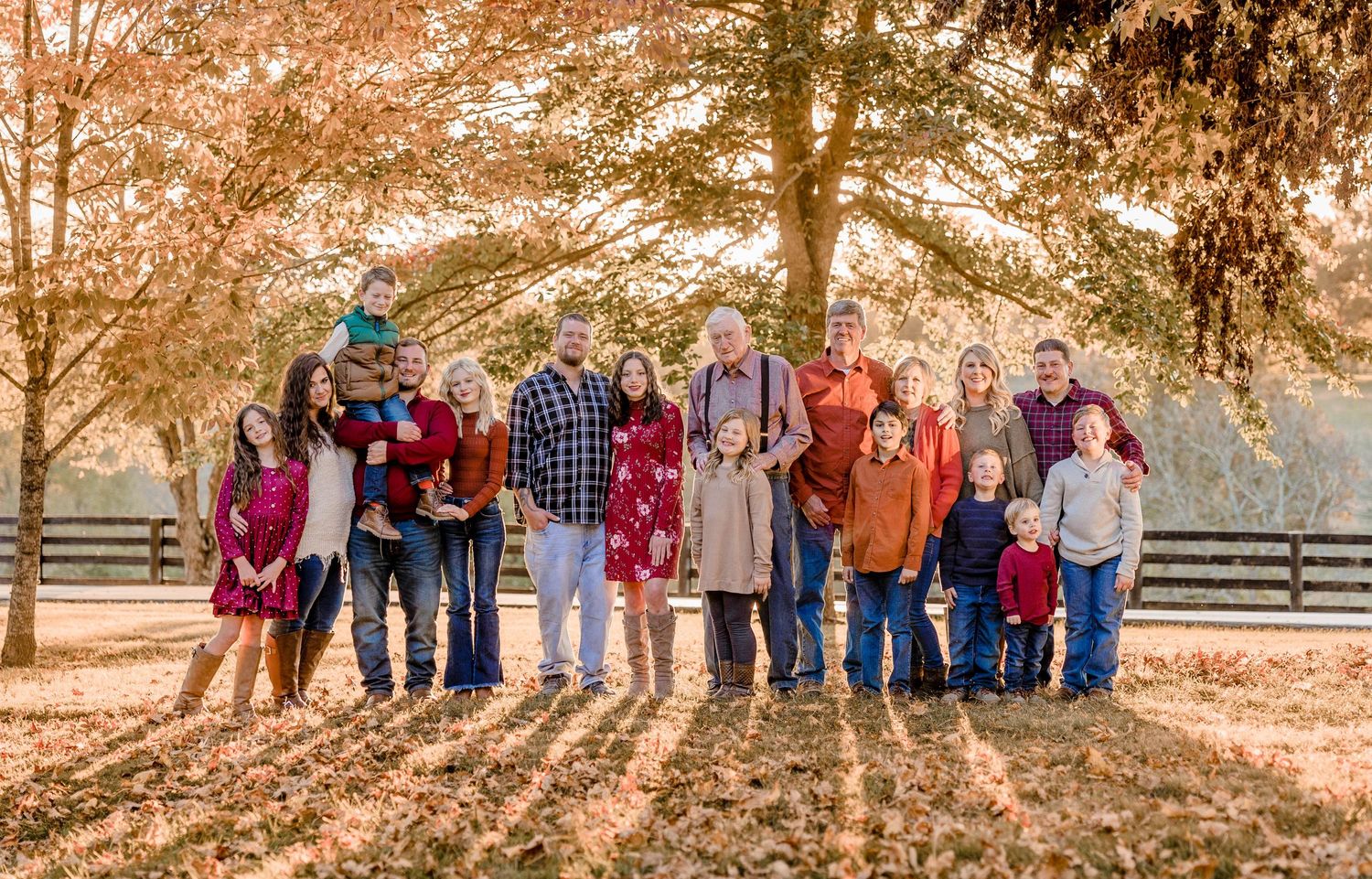 A large group gathering poses outdoors under colorful fall foliage and trees at sunset.
