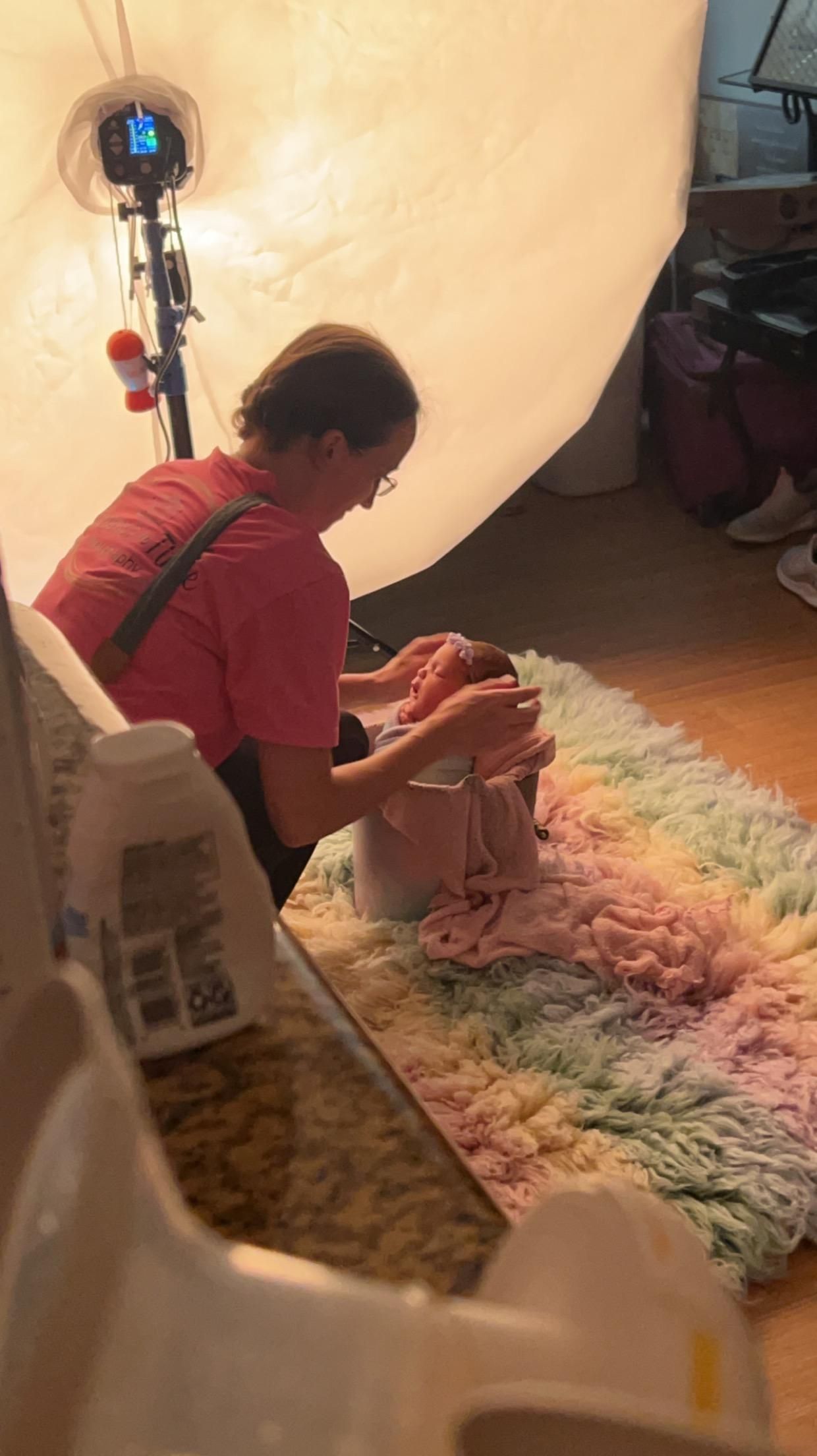 Photographer posing sleeping newborn baby in pink wrap on rainbow fluffy rug with professional studio lighting.