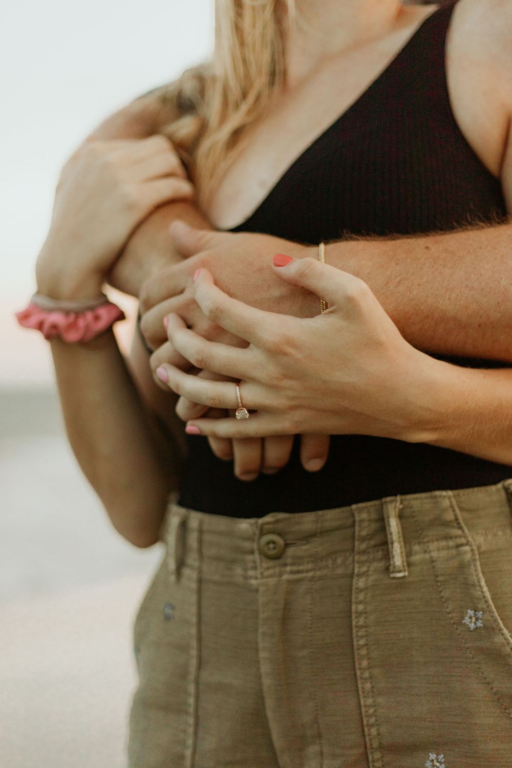 Close-up of intertwined hands with engagement ring on beach.