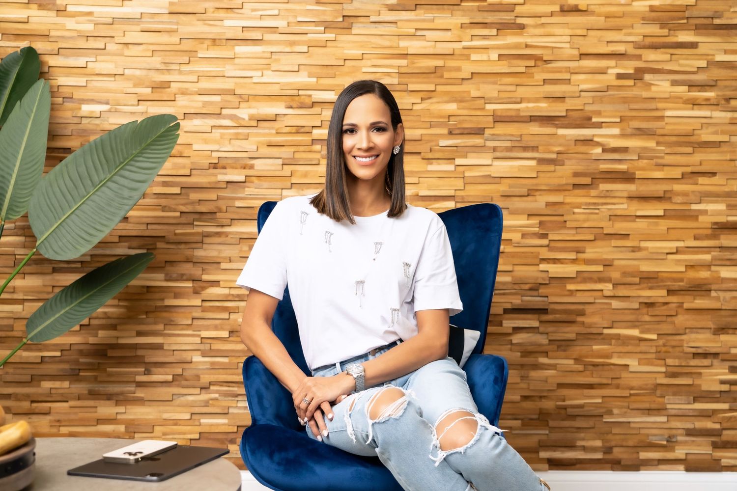 Casual professional sitting in blue chair against textured stone wall with tropical plant decor.