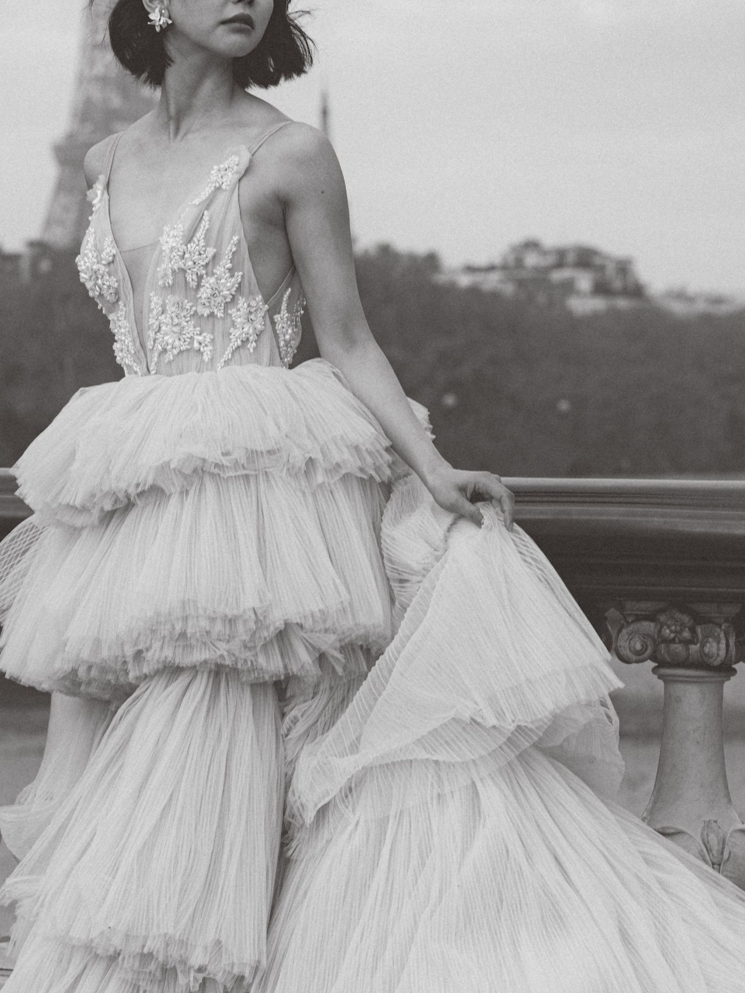Ethereal black and white photo of a layered tulle wedding gown with delicate lace details on a balcony.