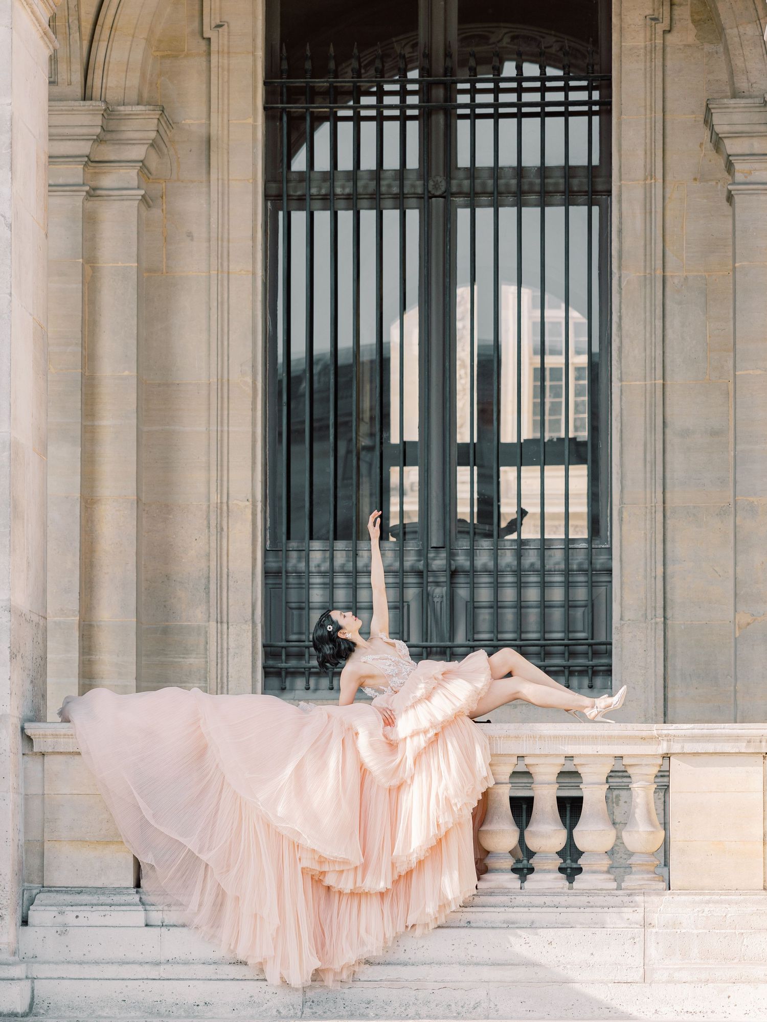Dreamy blush gown spread across classic architecture balcony with ornate iron gates.