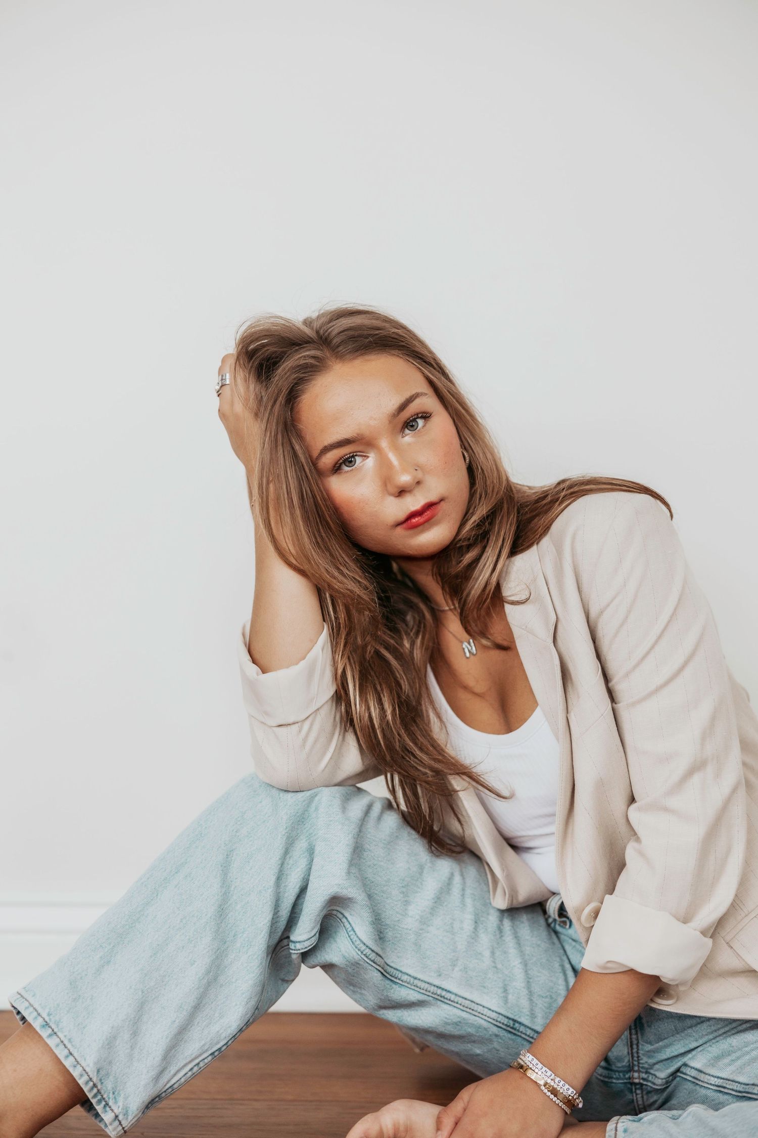 Casual lifestyle portrait in beige blazer and jeans against white wall.
