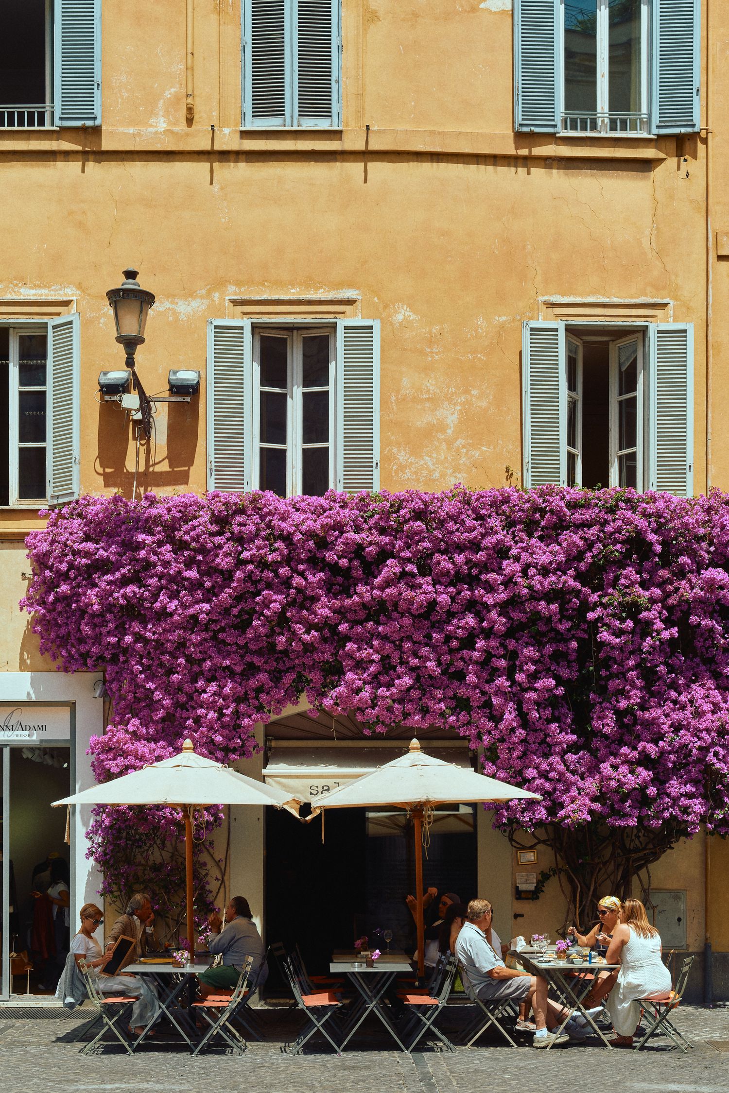 Cafe terrace with purple bougainvillea cascading down ochre building wall in Rome.