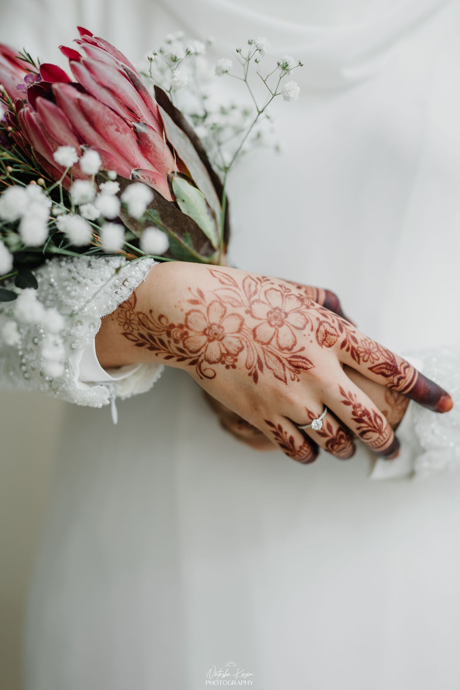 Close-up of henna adorned hands holding delicate white flowers and red blooms.