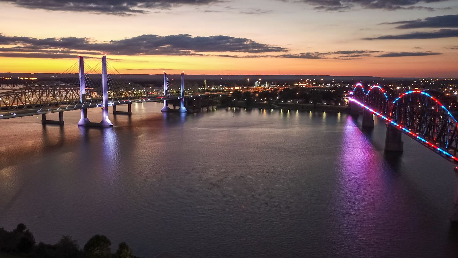 Panoramic sunset view of Louisville's skyline with the Ohio River and bridges illuminated in purple.