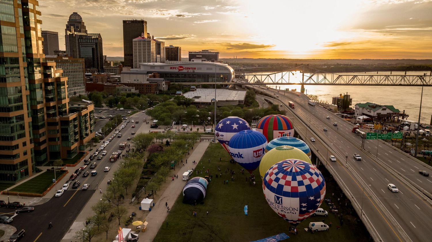 Aerial panorama of Louisville waterfront at golden hour with dramatic clouds and city buildings.