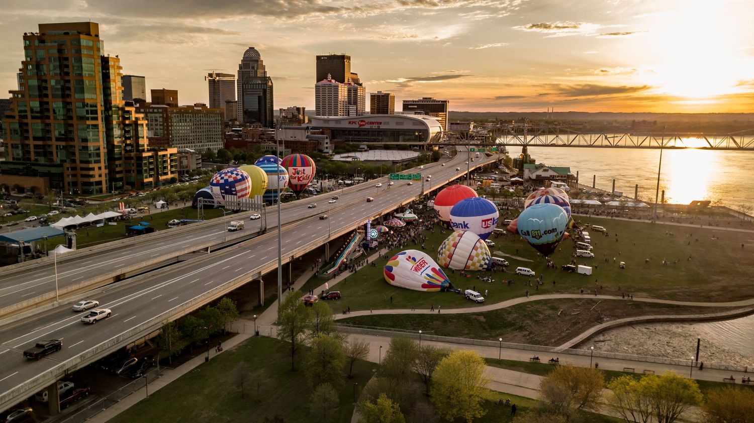Panoramic view of Louisville's riverfront with hot air balloons and urban landscape at sunset.