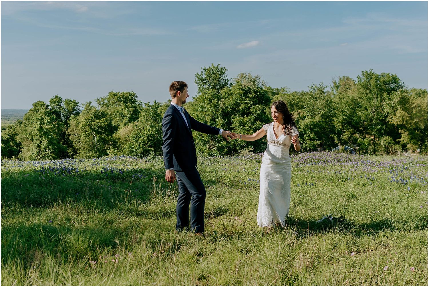 A couple holds hands while walking through a scenic hilltop meadow.