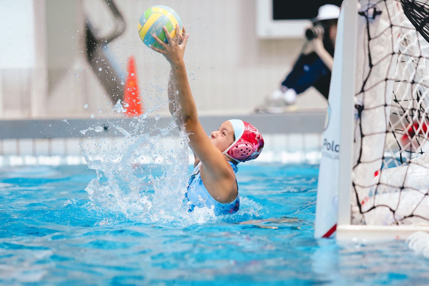 Water polo player reaches up to block a yellow ball during an intense pool match.