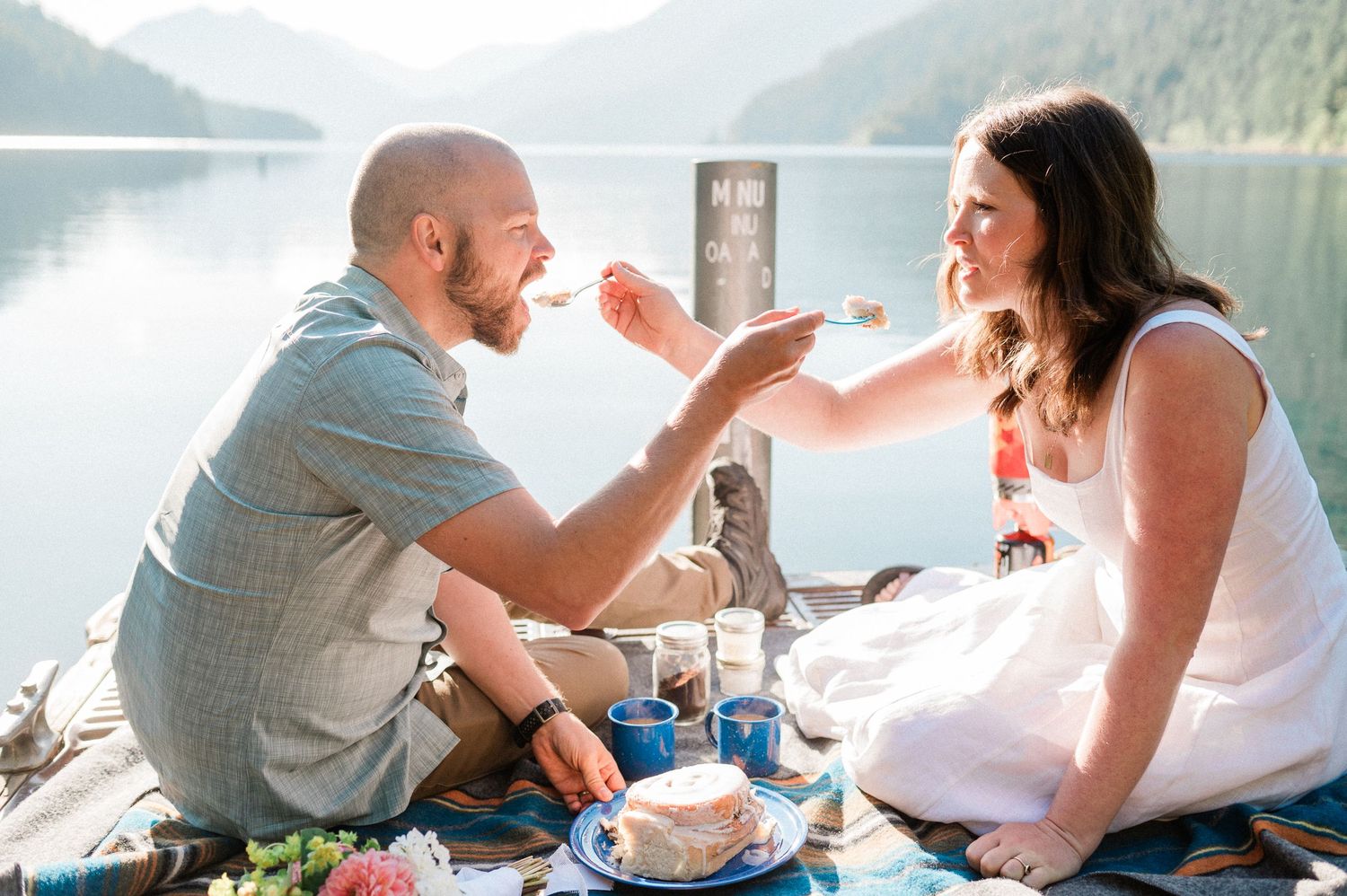 Bride ands groom feeding each other a big cinnamon roll during their Lake Crescent Elopement. Photo by Pine + Vow