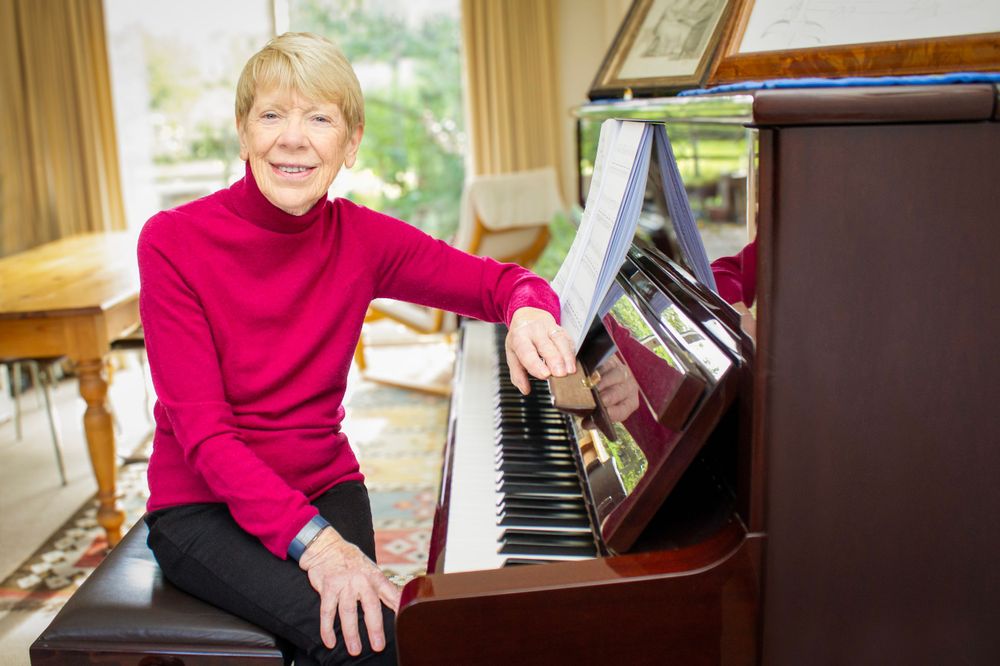 Piano teacher sat facing her piano. Environmental portrait.