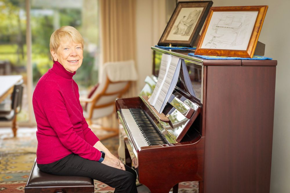 Piano teacher sat facing her piano. Environmental portrait.