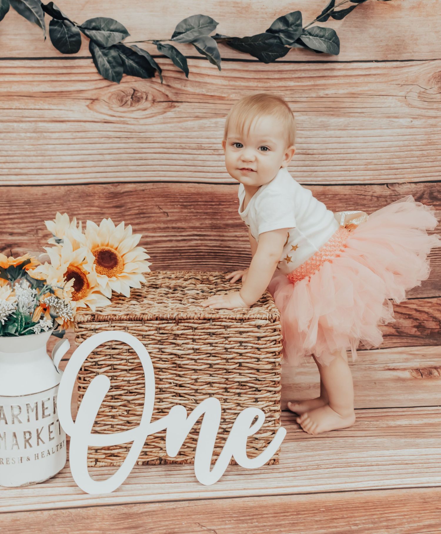 Baby in tutu with sunflowers and rustic decor during first birthday photoshoot.
