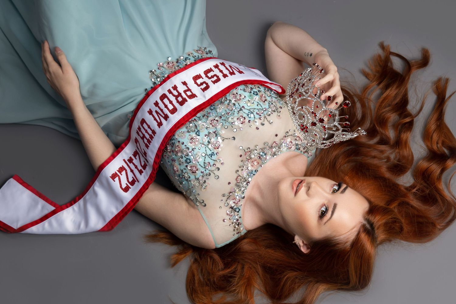 pageant queen laying on floor in green dress holding crown and sash across tummy