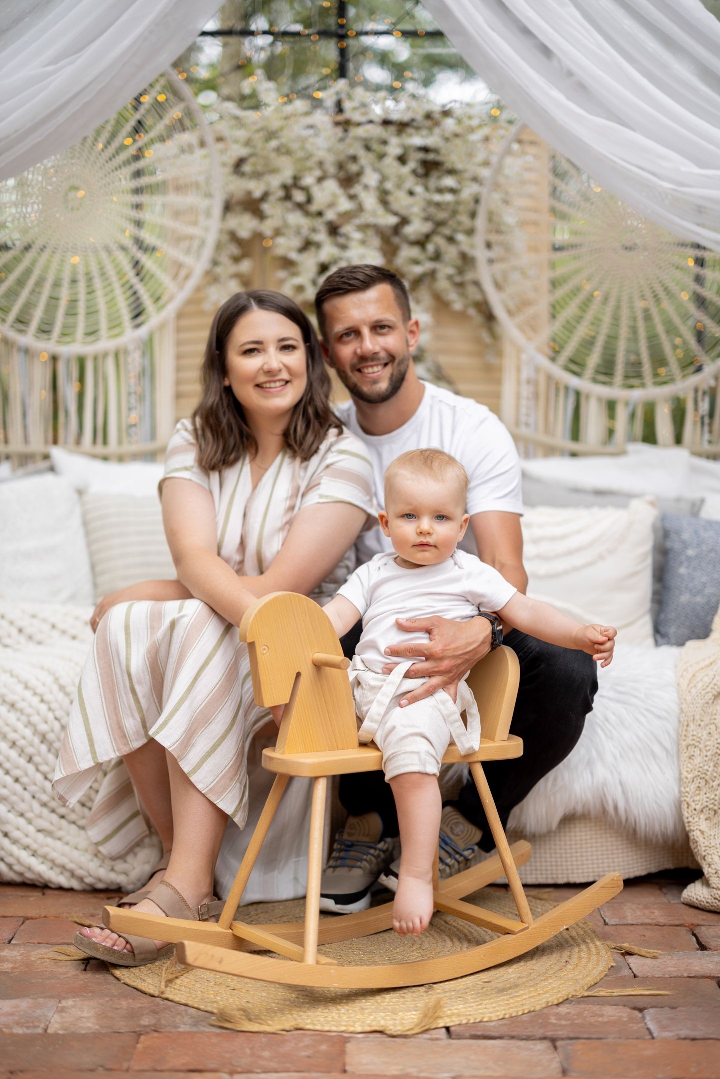 Family portrait with baby sitting on wooden rocking horse under decorative arch.