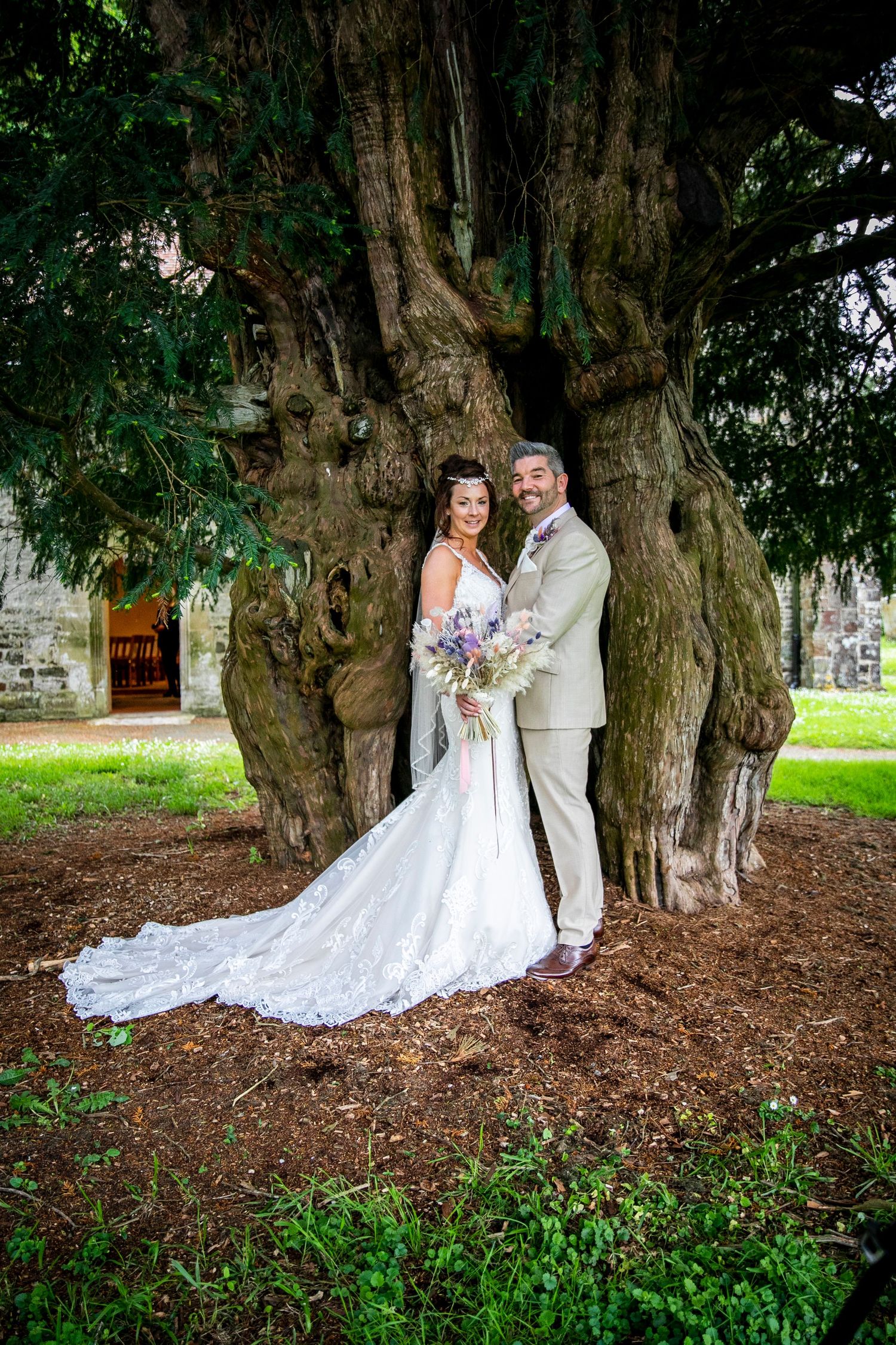 Wedding couple poses for romantic portraits under an ancient tree with trailing dress.