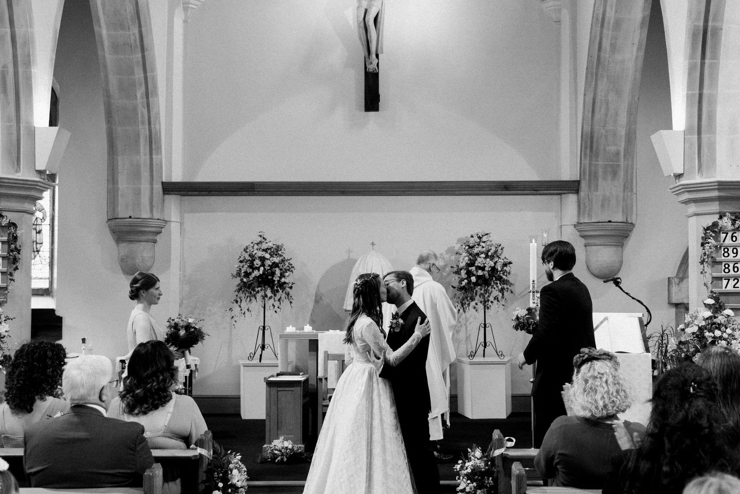 A wedding ceremony takes place in a traditional church with floral arrangements and guests in attendance.