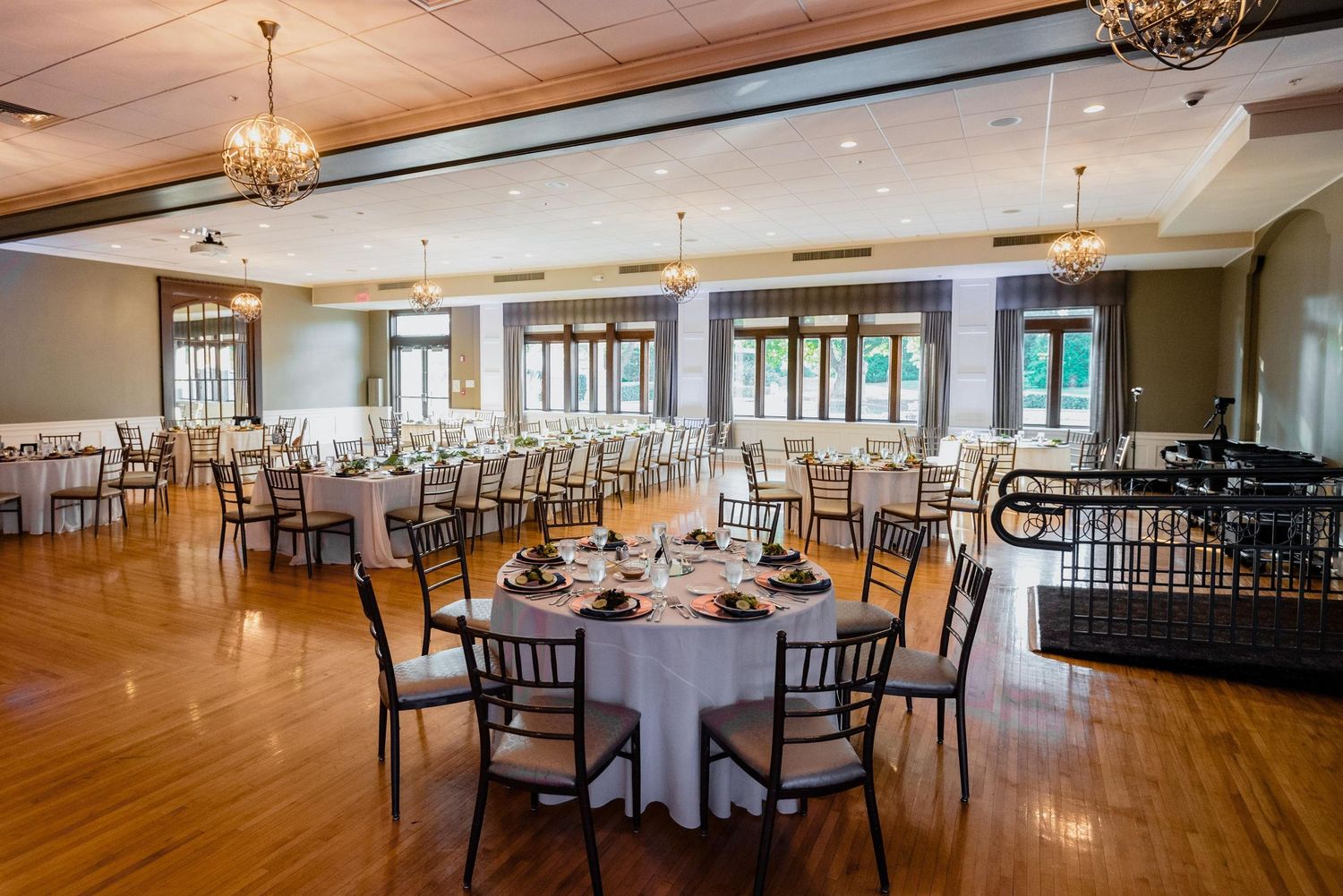 Spacious reception hall with dark wooden chairs and round tables arranged for a formal event.
