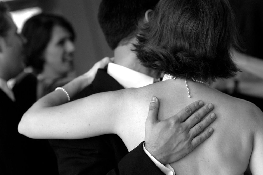 A black and white close-up photo of a couple embracing while slow dancing at a formal event.