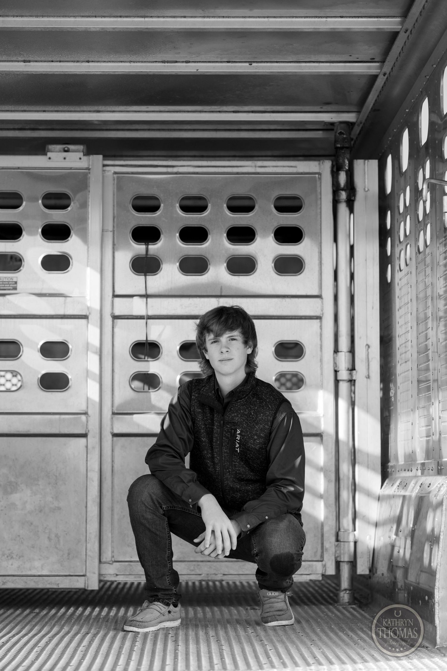 Black and white portrait inside livestock trailer shows casual pose against ventilated wall.