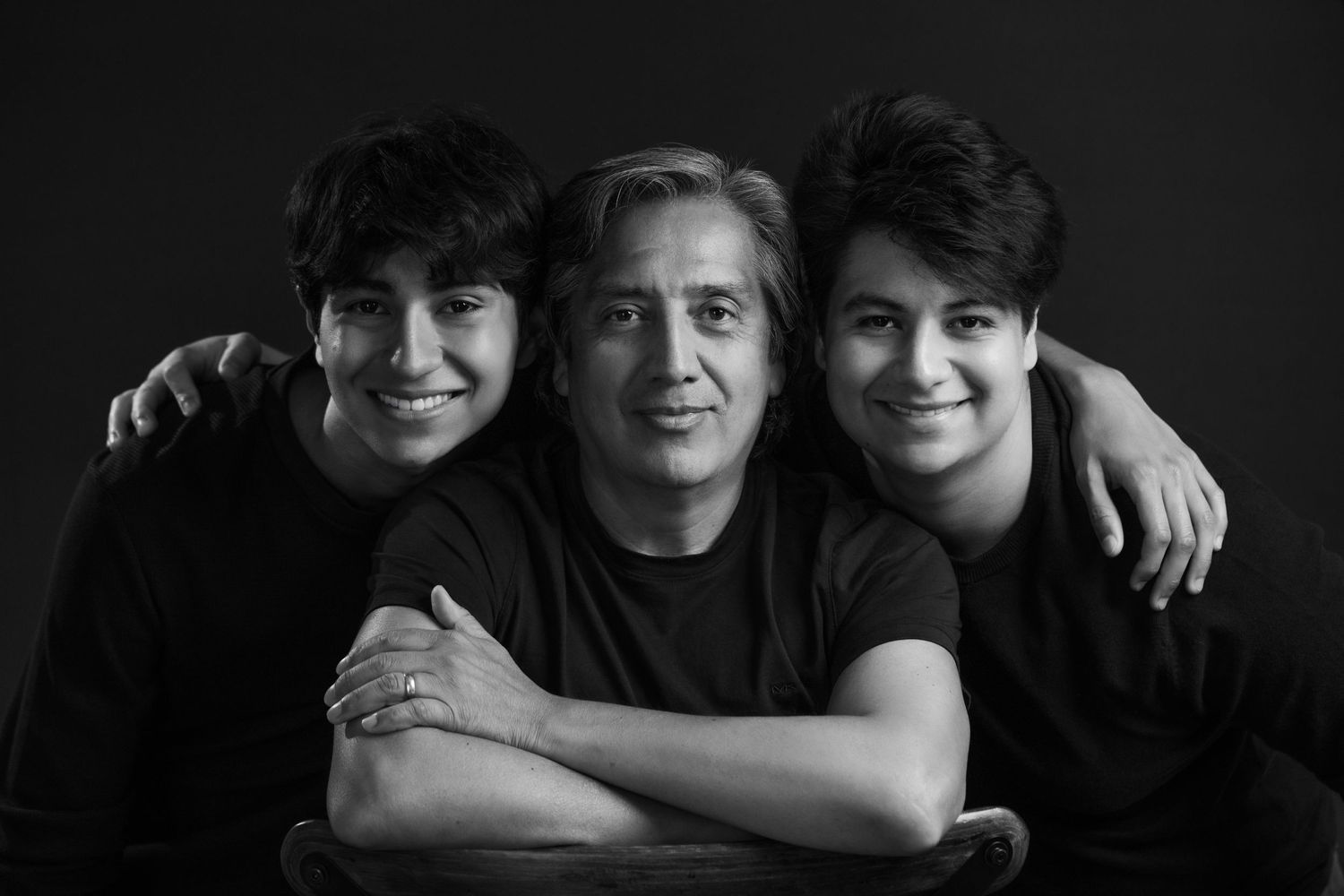 Black and white portrait of three people posing together against dark background.