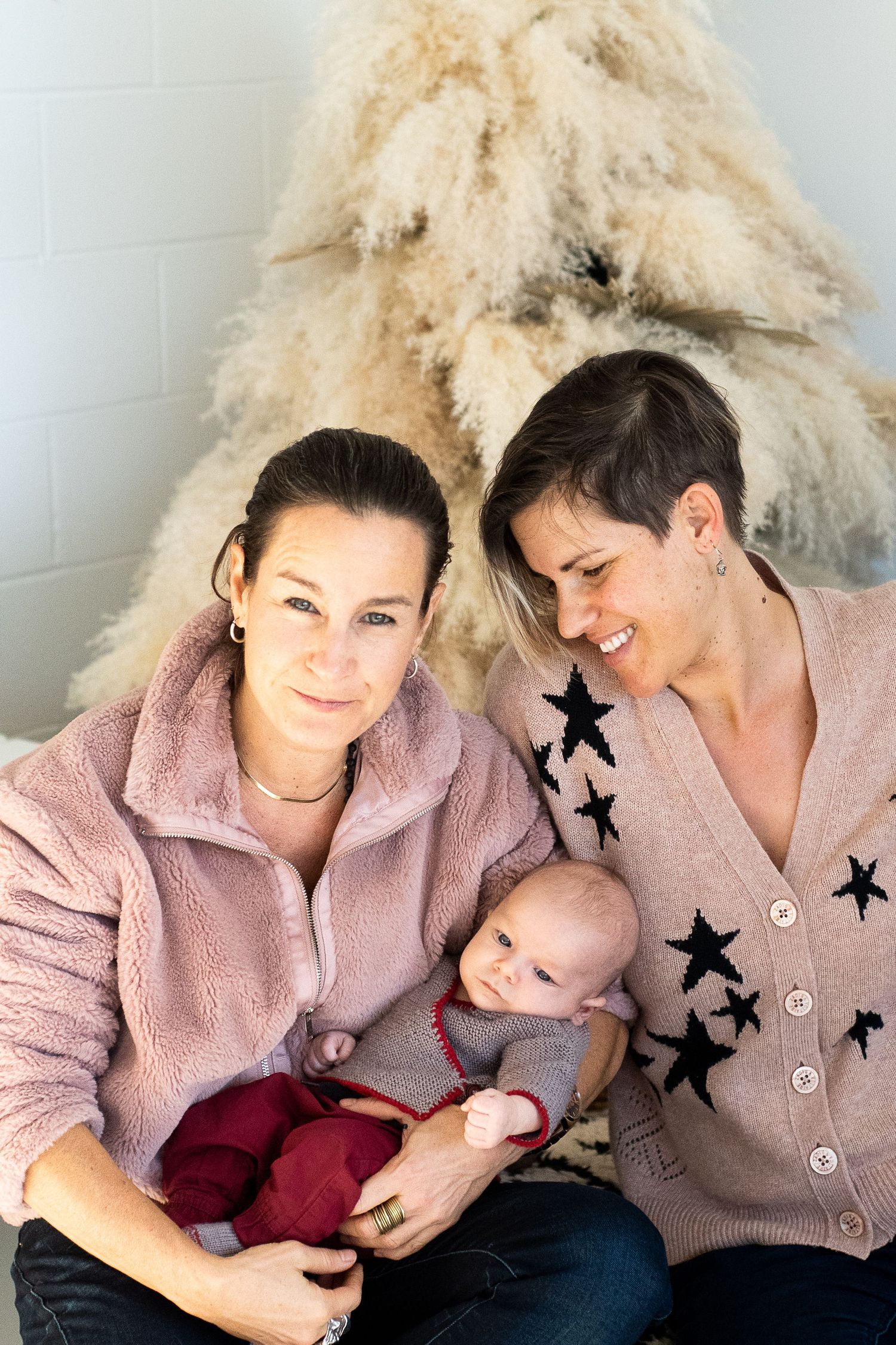Cozy family moment in front of pampas grass decoration wearing pink and star-patterned sweaters.
