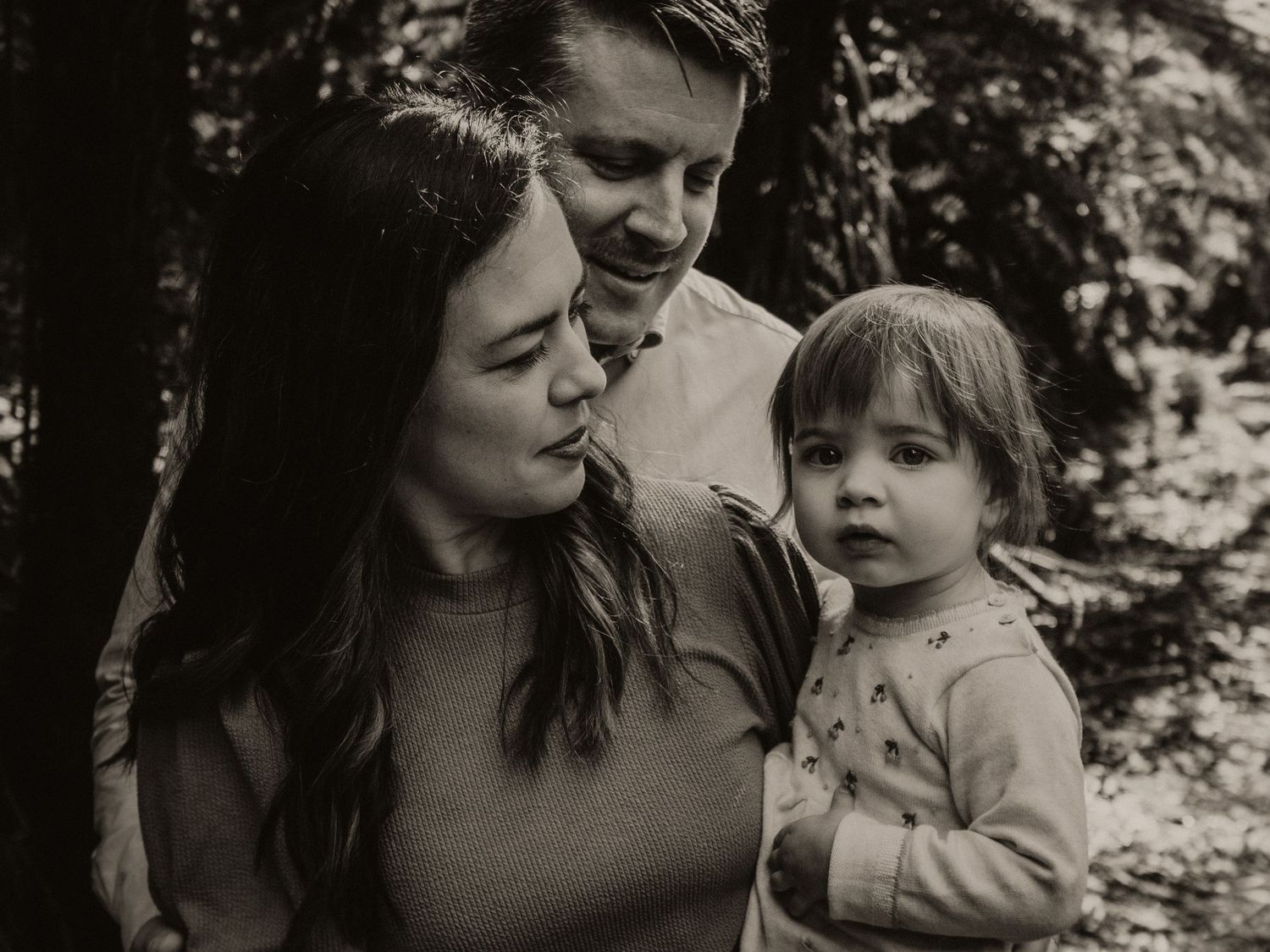 Mother and father looking at their toddler daughter whilst she looks at the camera