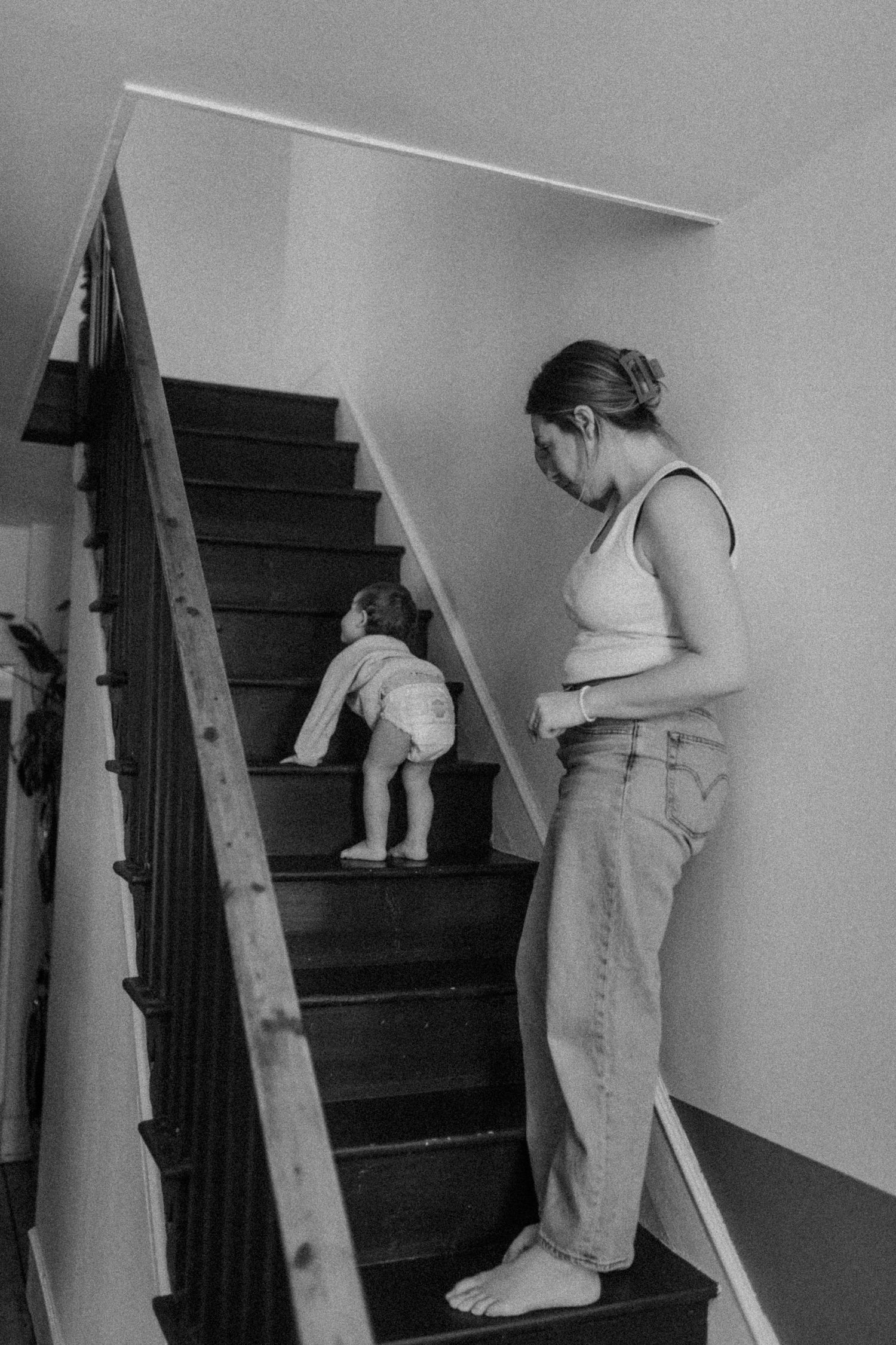 Black and white image of a parent supervising a small child climbing wooden stairs.
