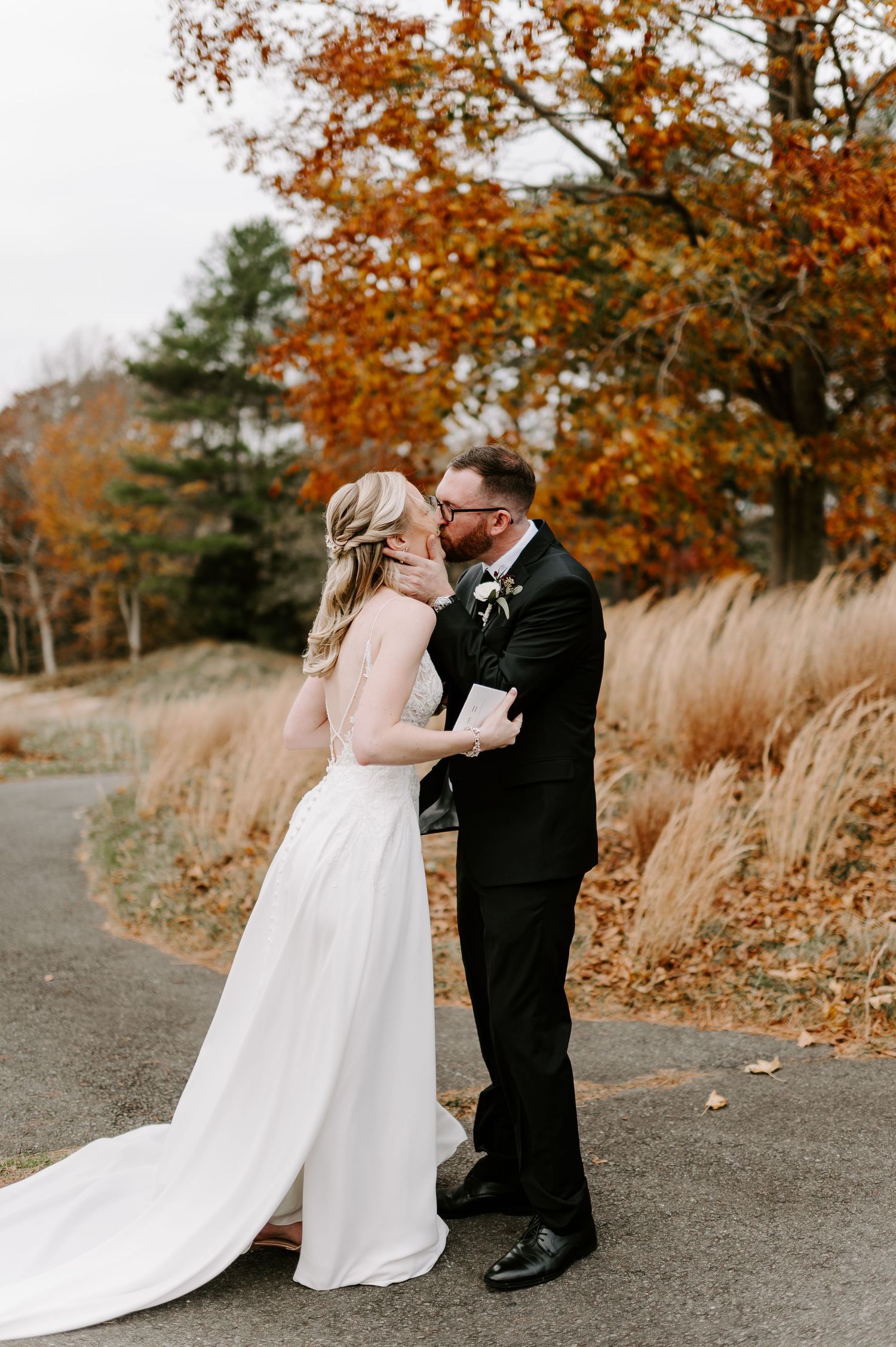 A couple shares an intimate moment on a gravel path with golden autumn trees in the background.