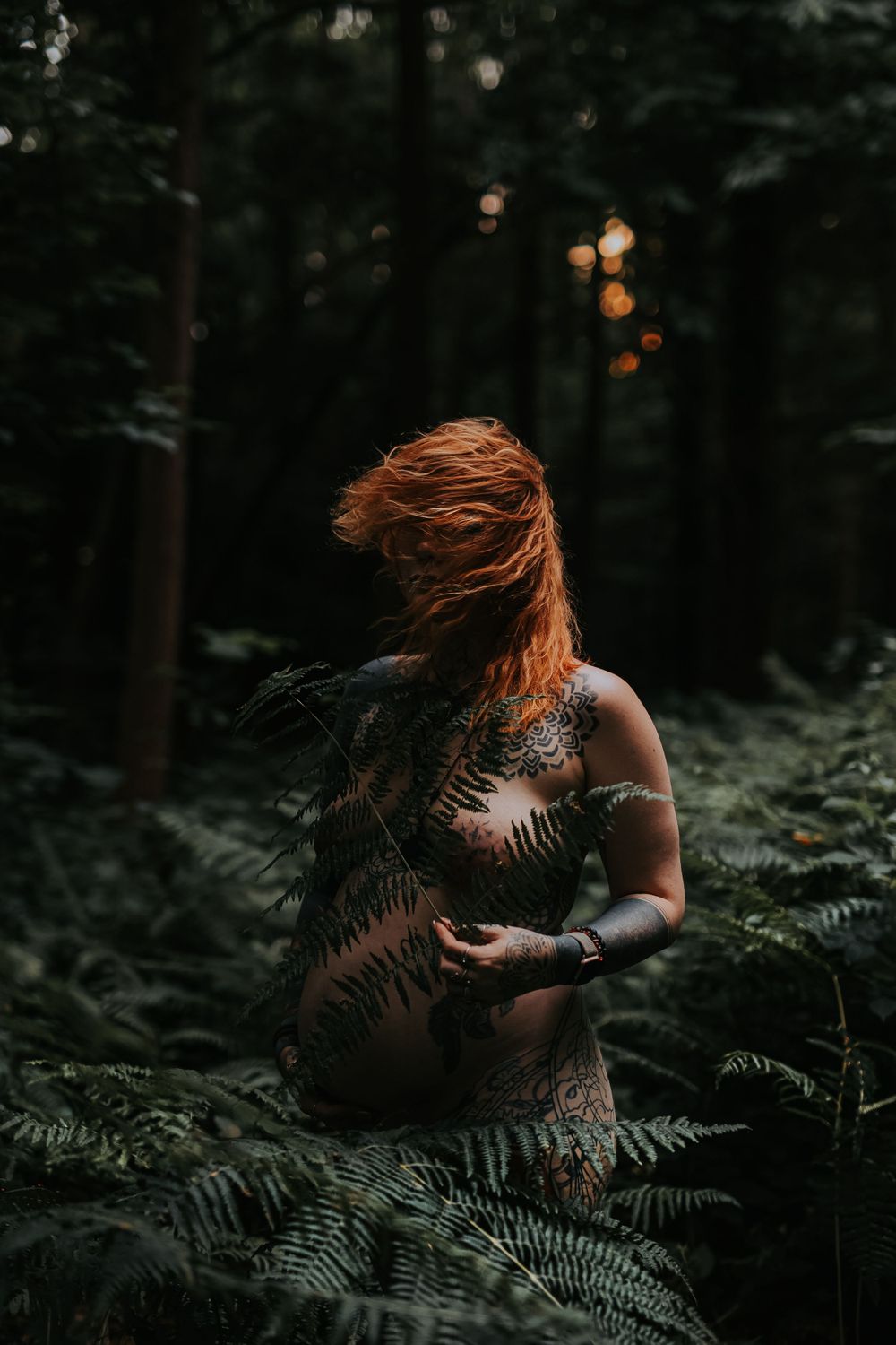 A moody forest portrait with a person surrounded by ferns in dappled sunlight.