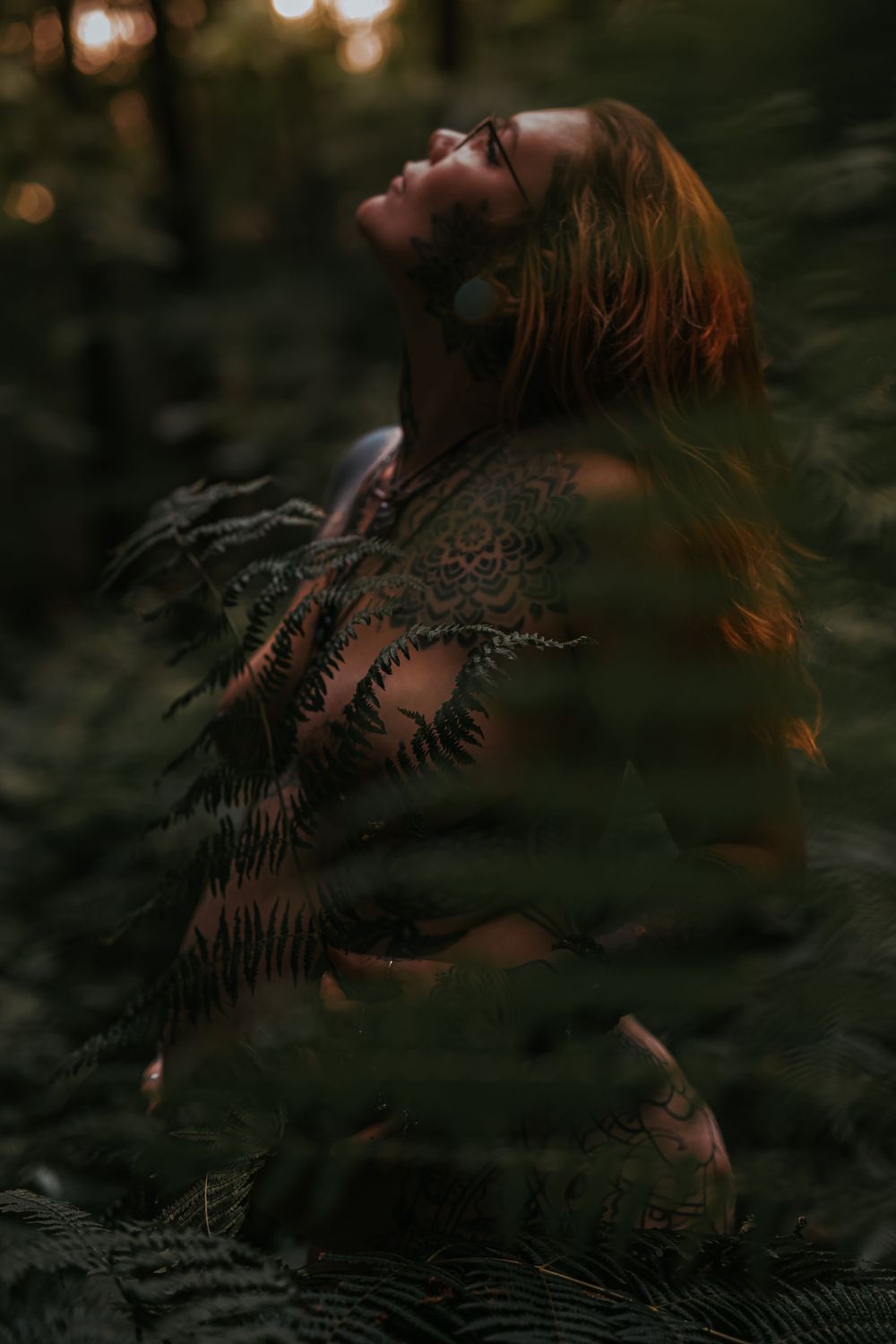An artistic portrait in a dark forest with fern shadows and golden light.