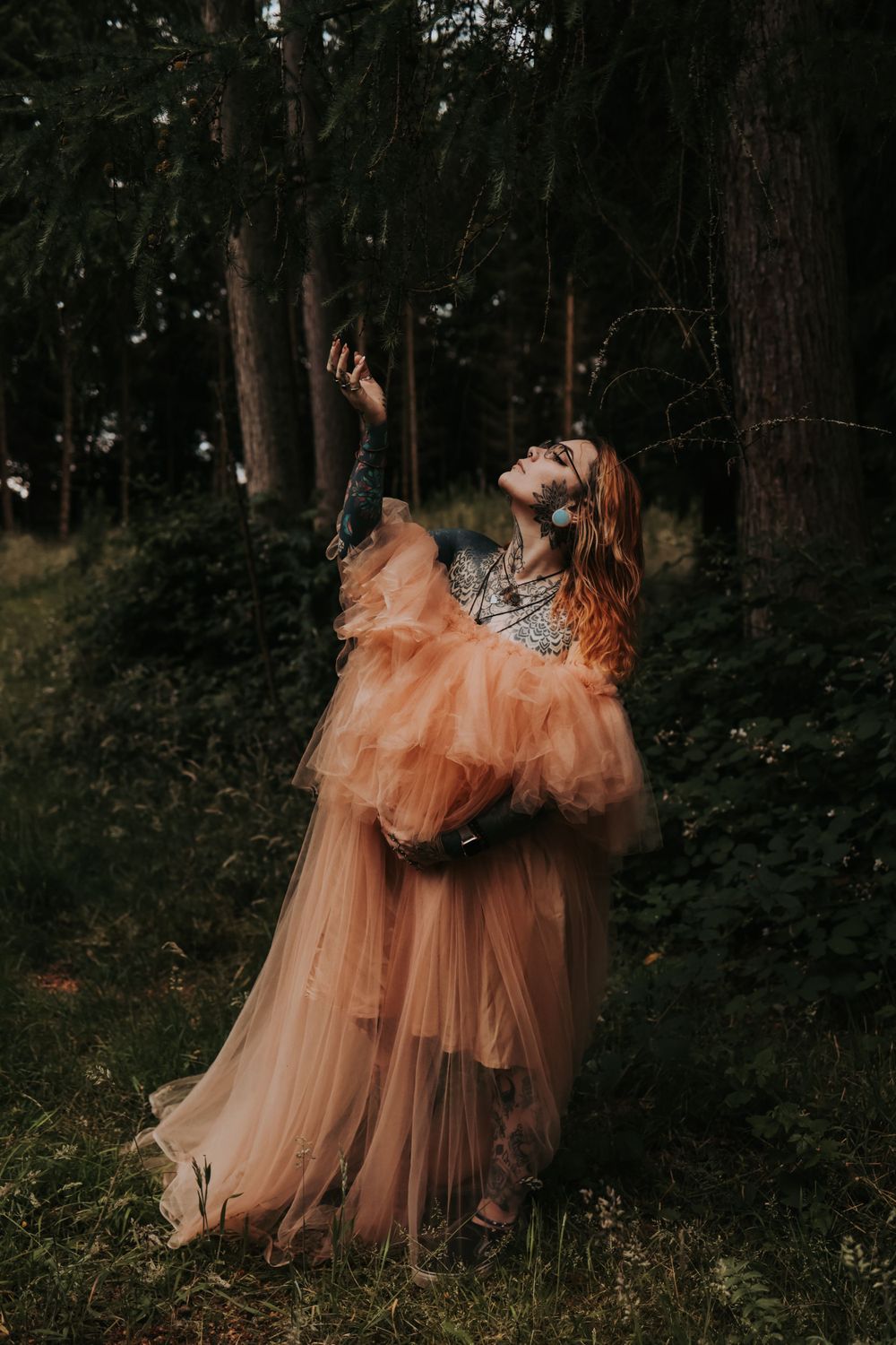 A flowing peach tulle gown creates an ethereal silhouette against a dark forest backdrop.