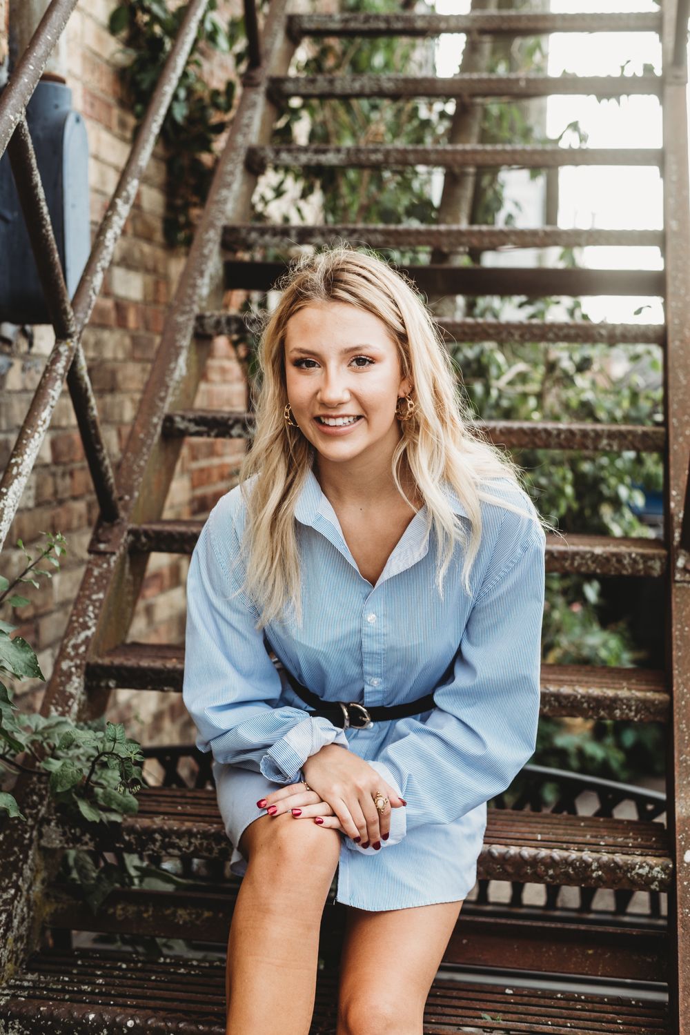 Woman in light blue shirt sitting on vintage metal bench outdoors.