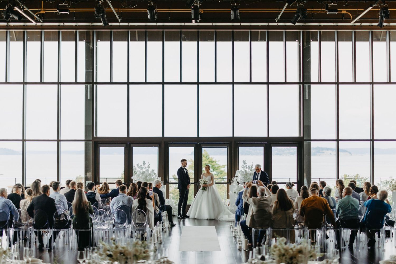 Modern wedding ceremony in a bright industrial venue with floor-to-ceiling windows.