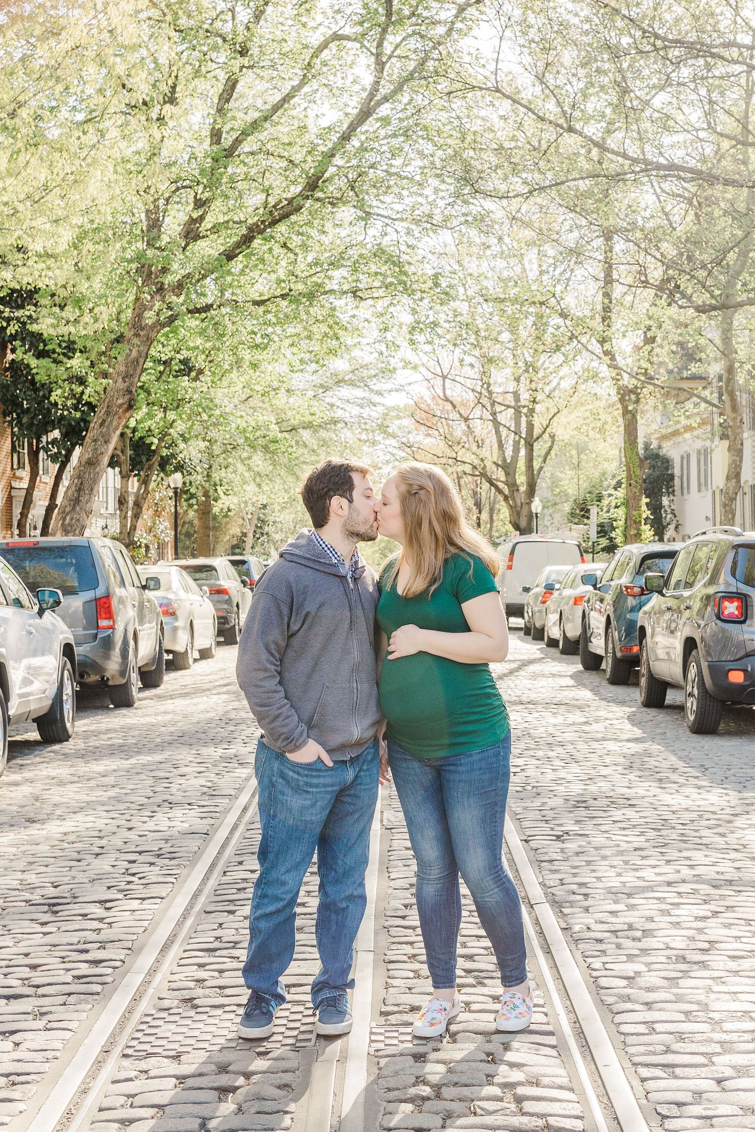A couple walks together on a tree-lined cobblestone street.
