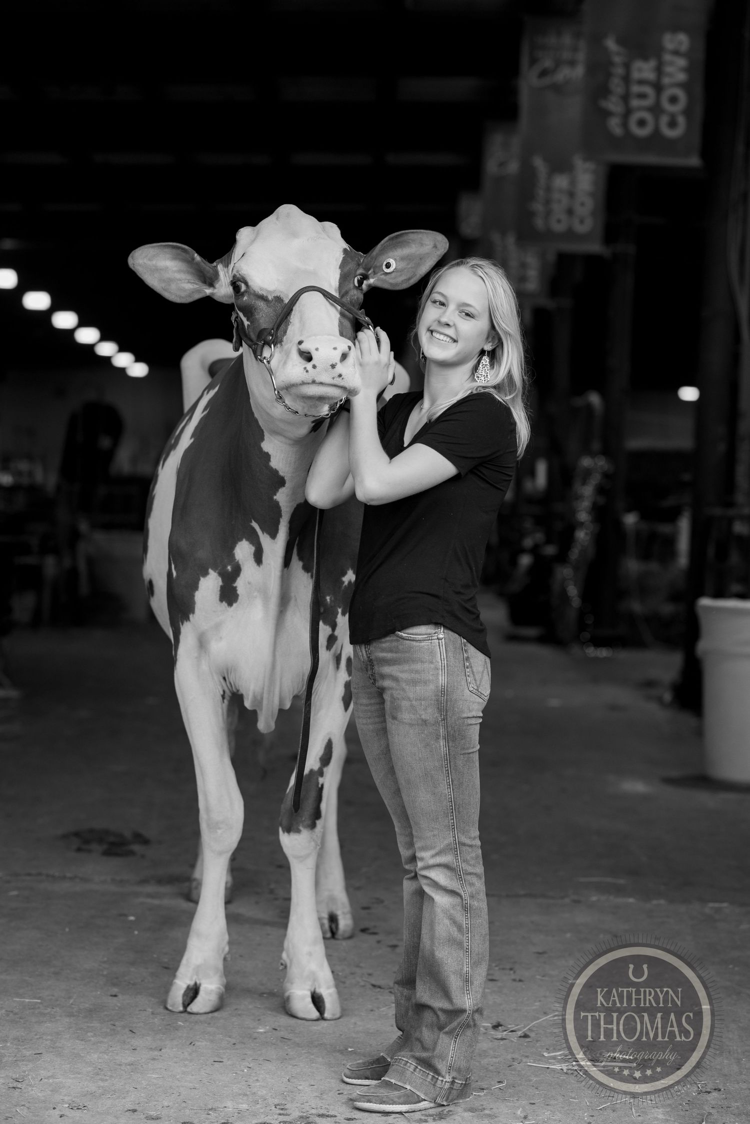 A black and white image captures a dairy cow and handler posing together at an indoor agricultural show.