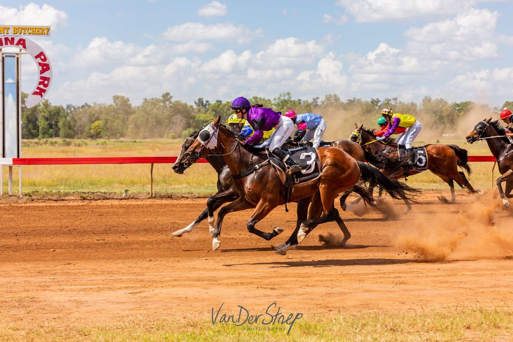 Racehorses in full gallop during intense race on red dirt track.