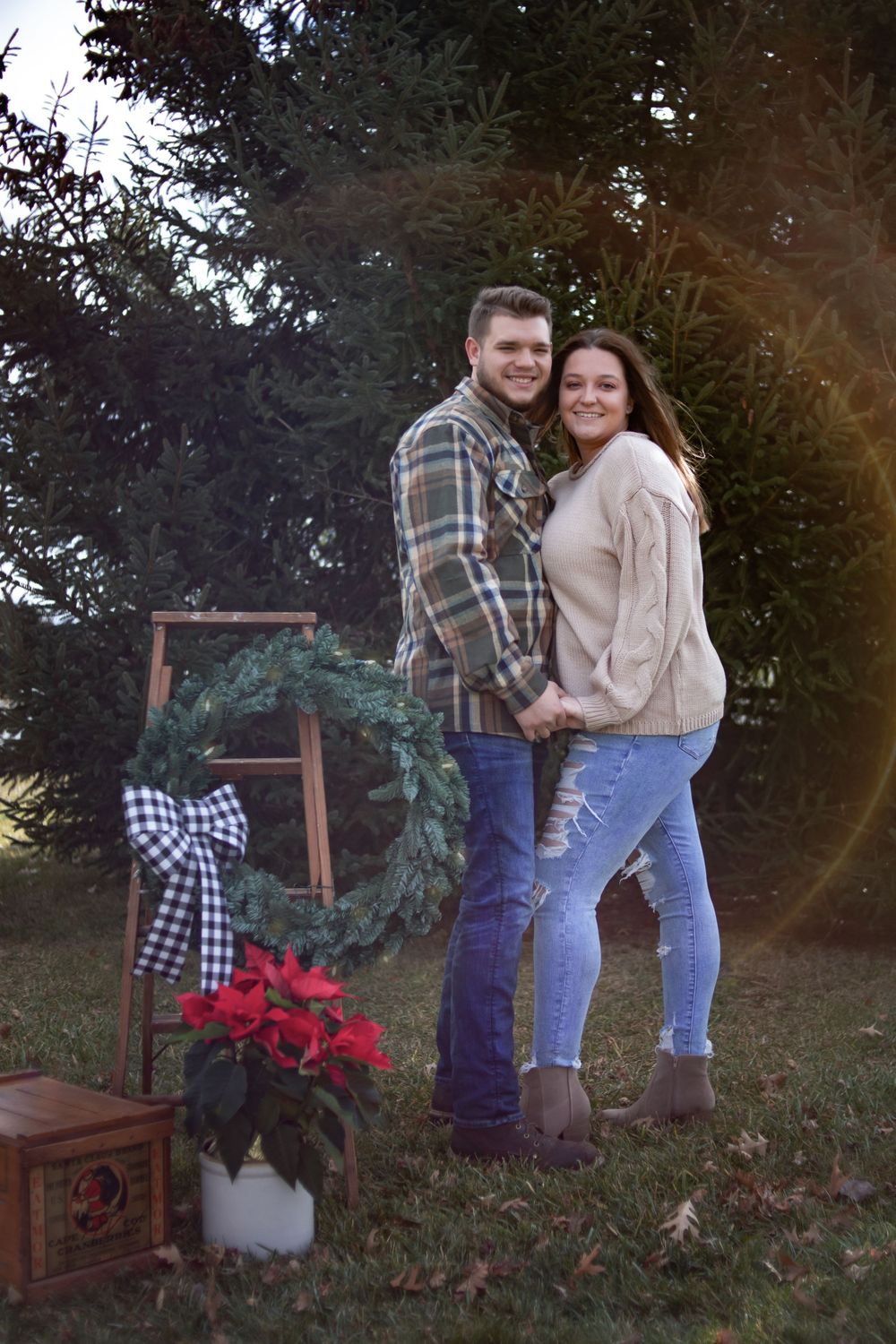 An outdoor holiday scene with a decorative wreath, poinsettia, and plaid accents at sunset.