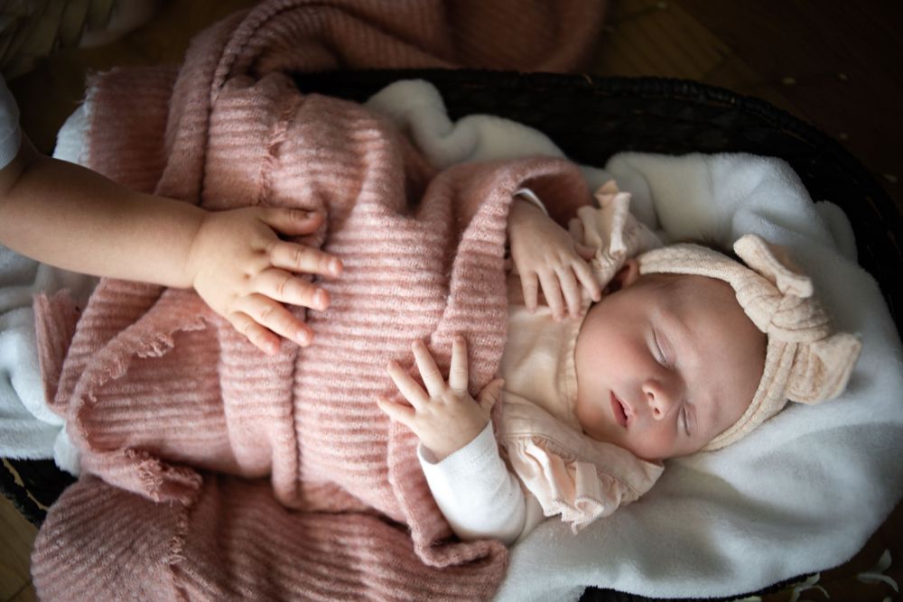 A sleeping newborn baby wrapped in a soft pink blanket with delicate lace details.