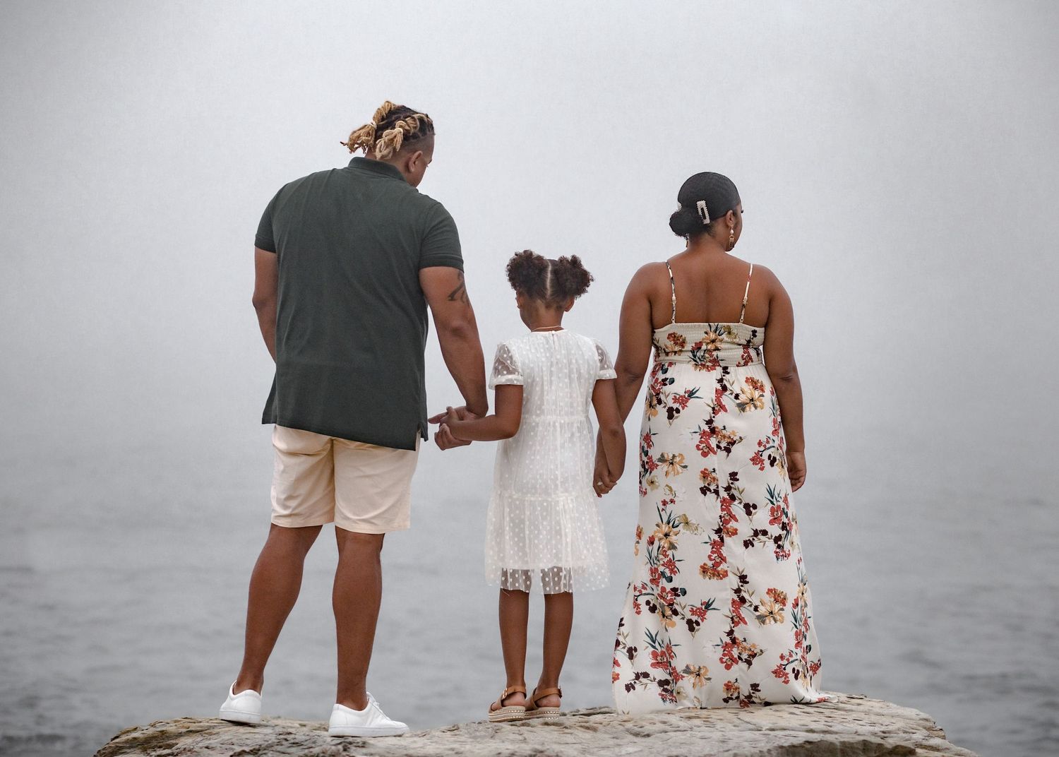 Couple in casual attire stands together on a rocky beach looking out at the misty ocean view in Jamestown, RI at Beavertail.