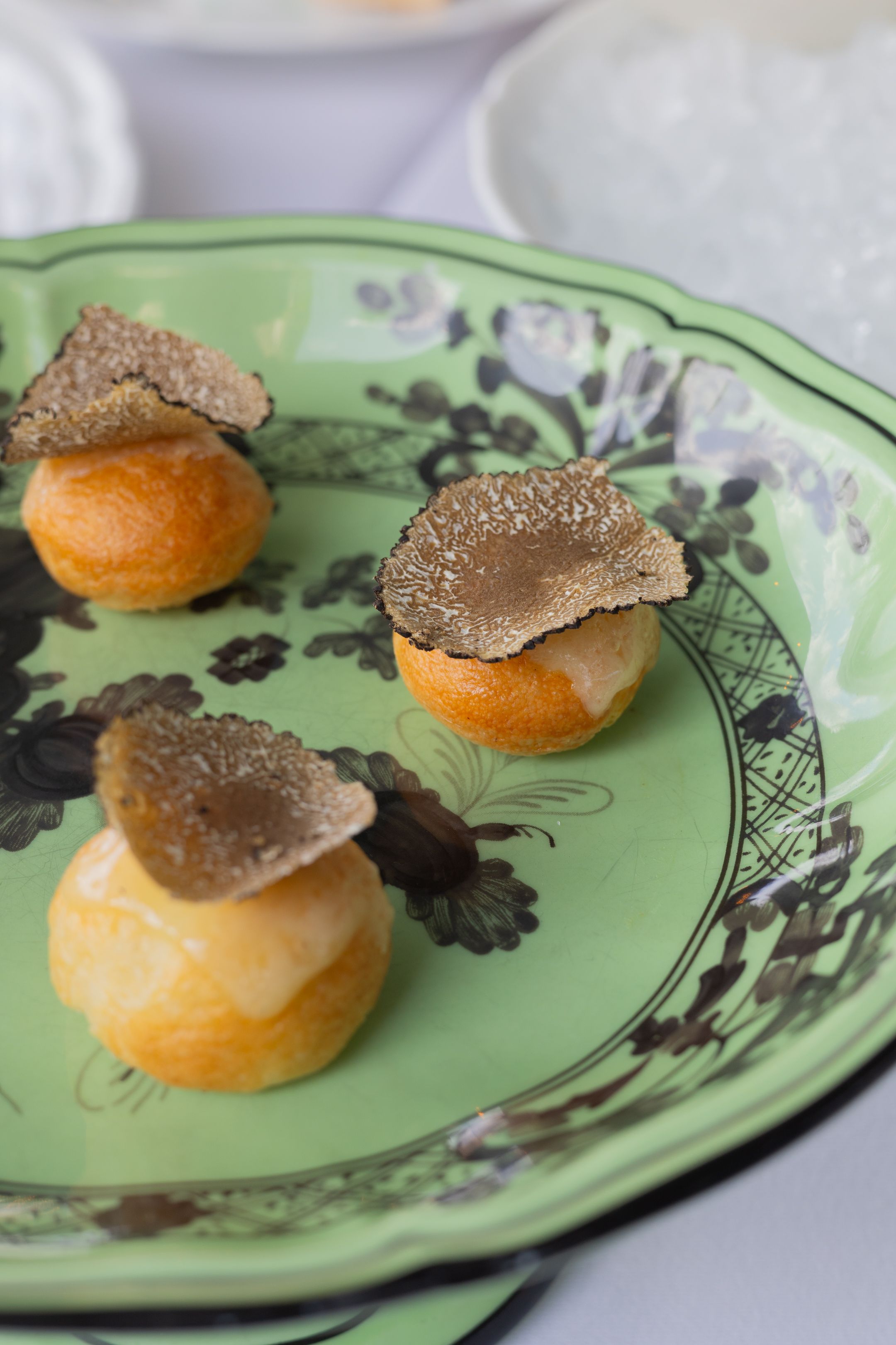 Elegant cream puffs topped with shaved black truffles served on a decorative green and white china plate.