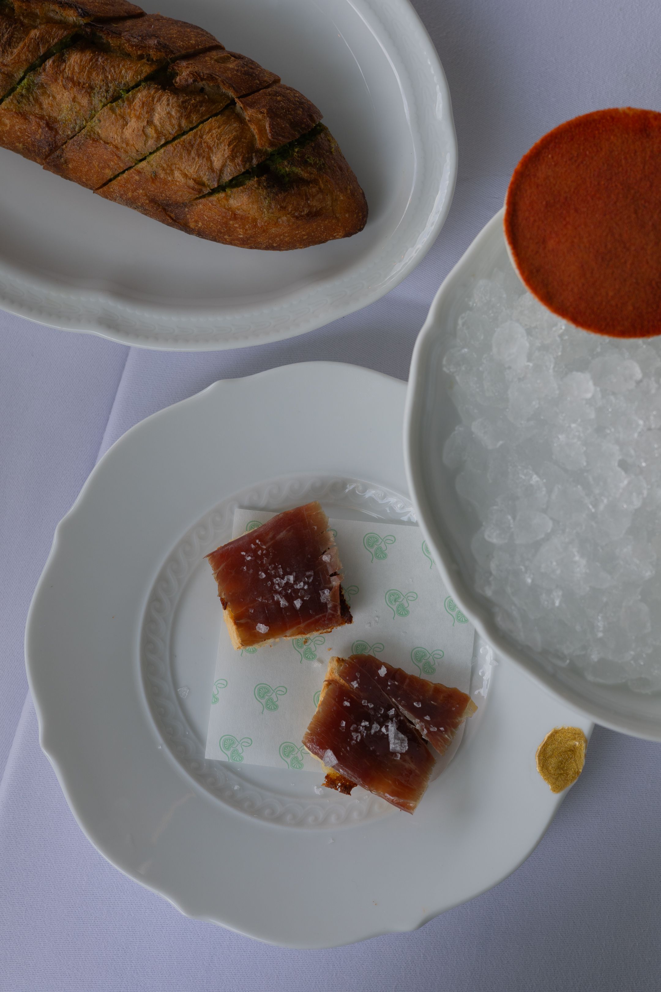 Plated dessert featuring caramel squares with sea salt, crushed ice, and a sliced rustic bread loaf on white dishes.