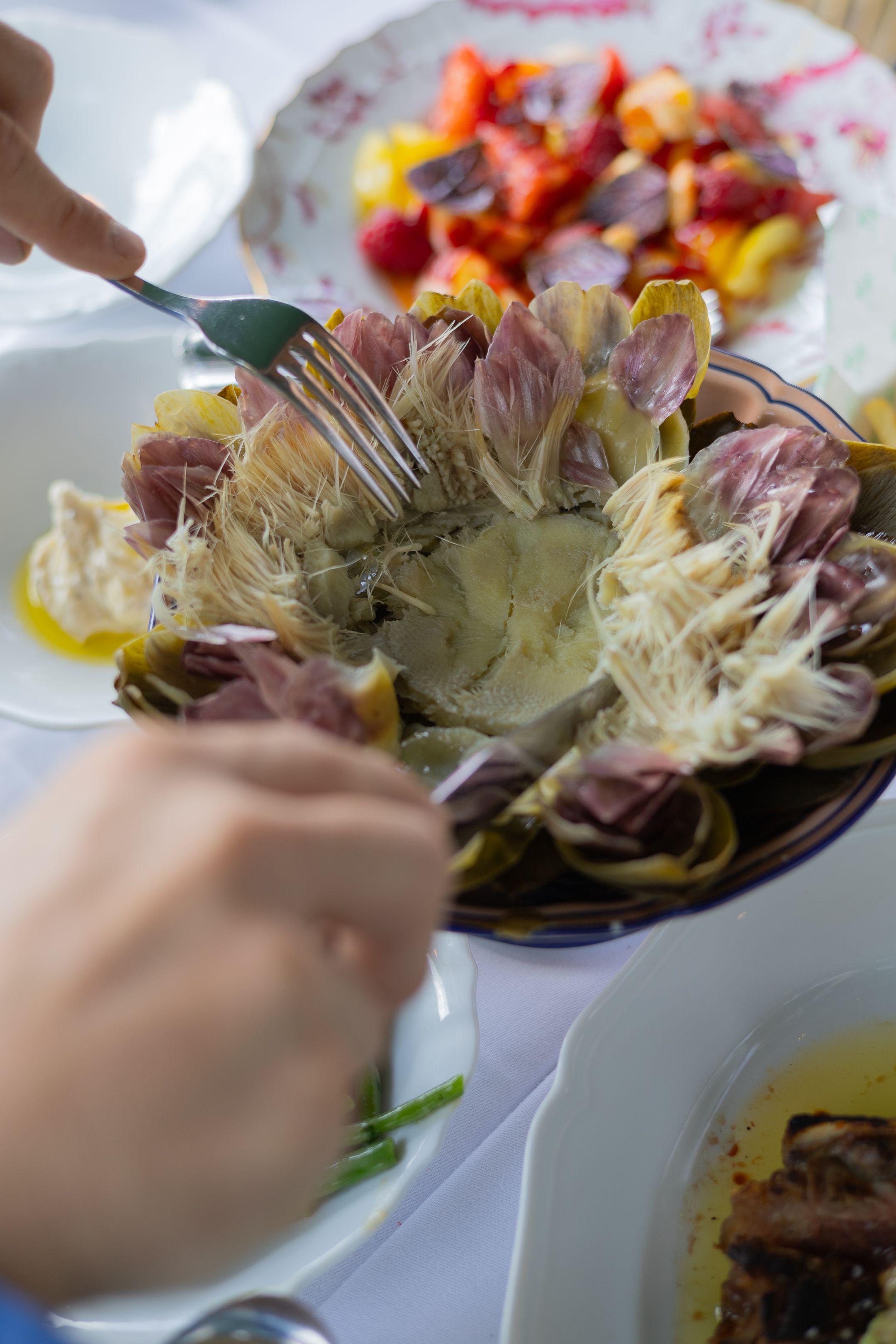 Hands using fork and knife to cut into a radicchio salad with colorful fruit dish visible in background.