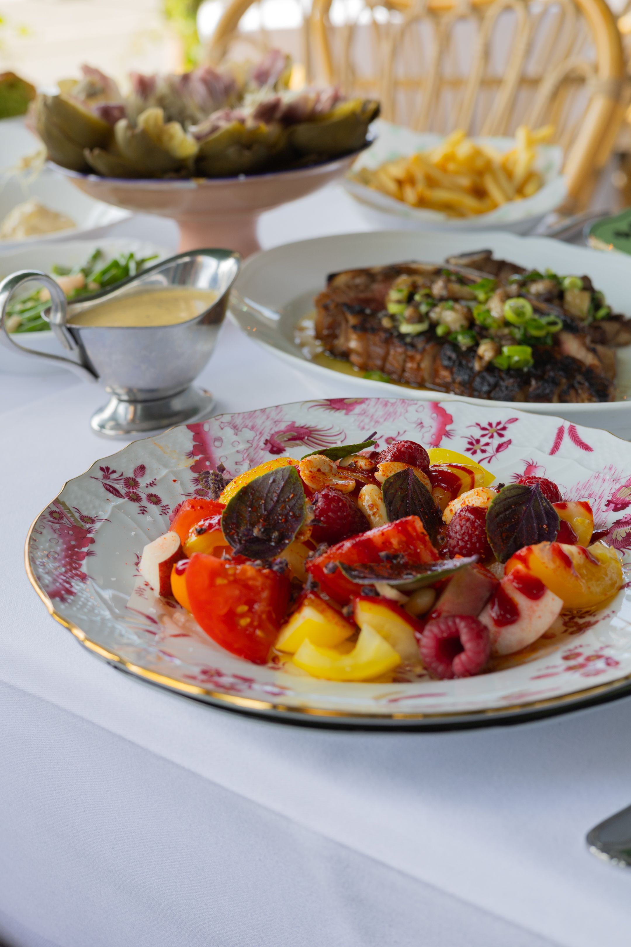 Colorful beet salad with tomatoes and citrus fruits served alongside steak and creamy sauce on elegant patterned plates.