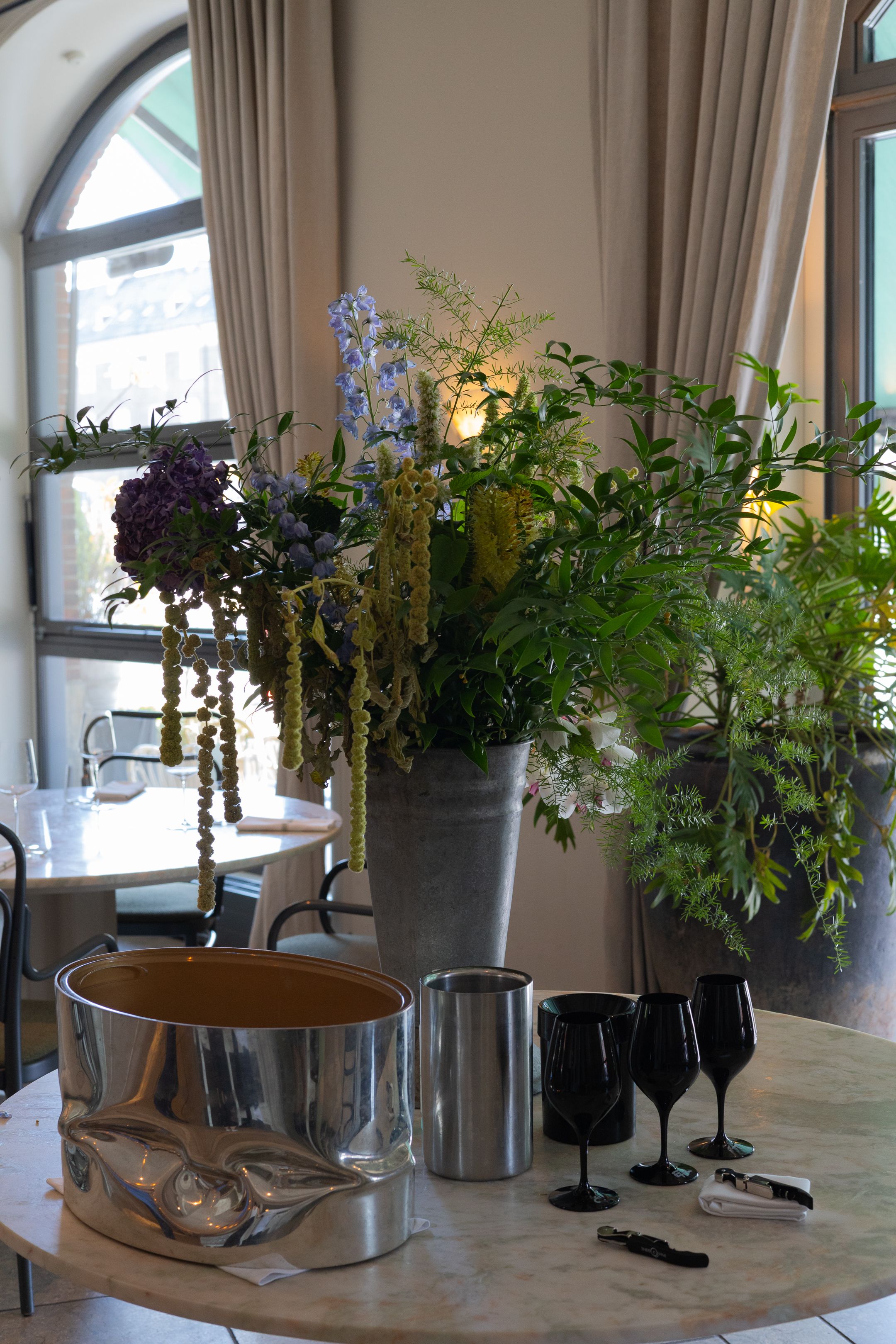 Elegant table setting with floral arrangements, black wine glasses, and metallic serving pieces near a large window.