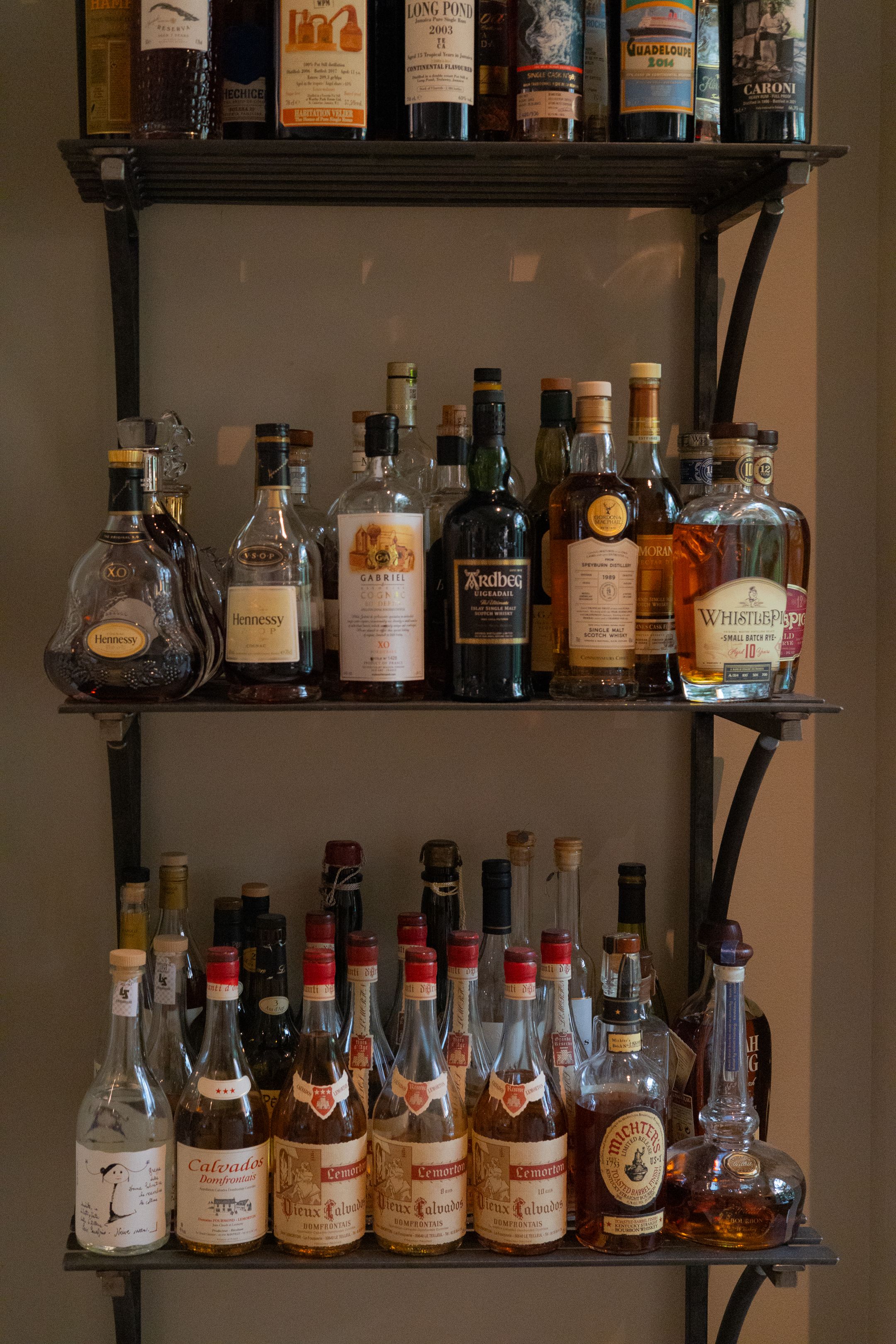 Three-tiered bar shelf displaying an extensive collection of liquor bottles and spirits.